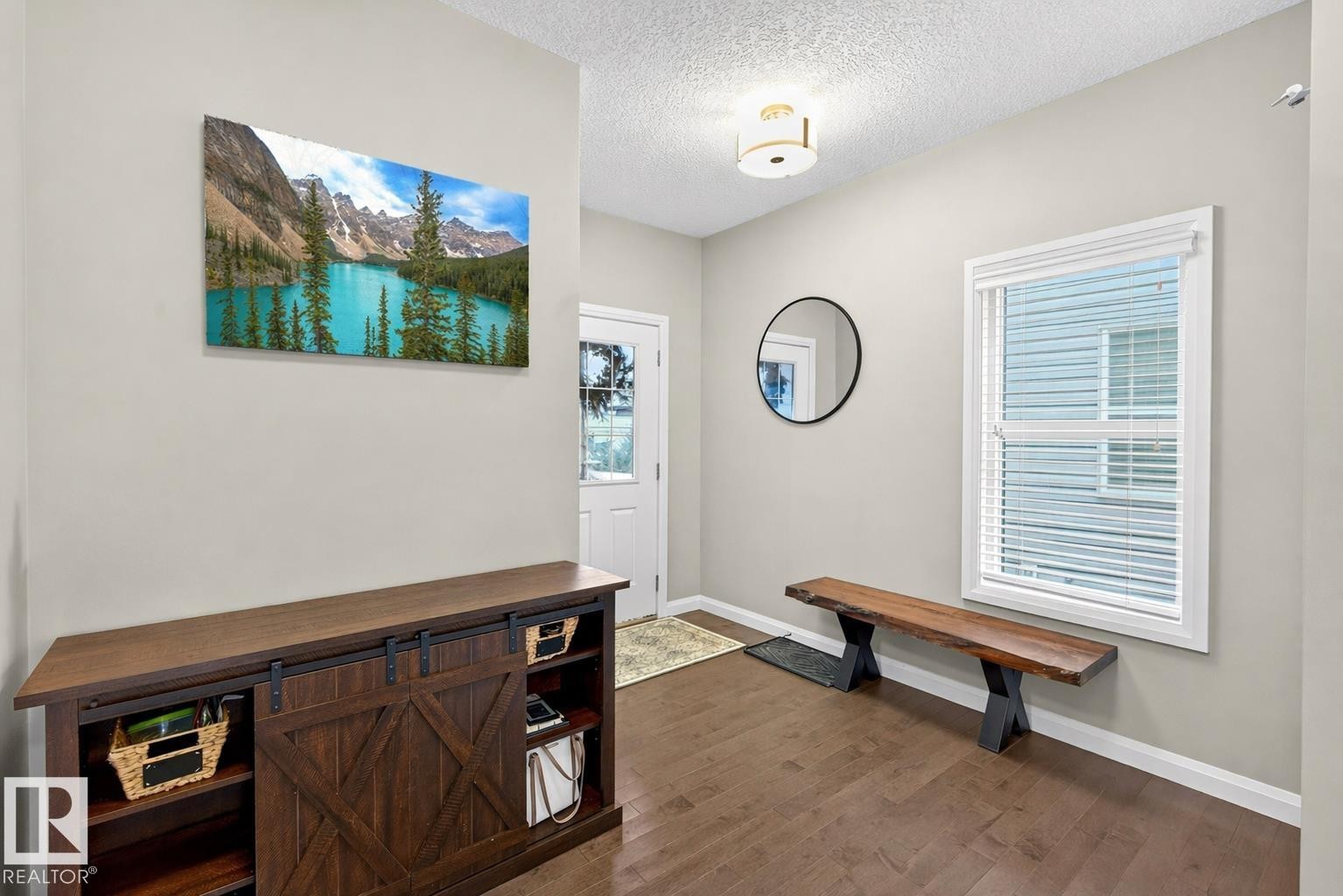 This inviting entryway features rich hardwood floors, neutral wall colors, a window with blinds providing natural light, and a white entrance door with a glass insert - 17838 60A Street, Edmonton, AB - Indoor Photo Showing Other Room