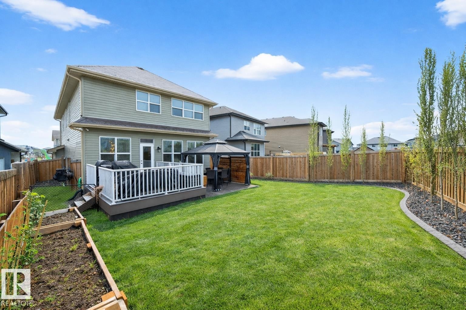 The property features a spacious backyard with a well-maintained lawn, a raised garden bed, and a wooden fence - 17838 60A Street, Edmonton, AB - Outdoor With Deck Patio Veranda