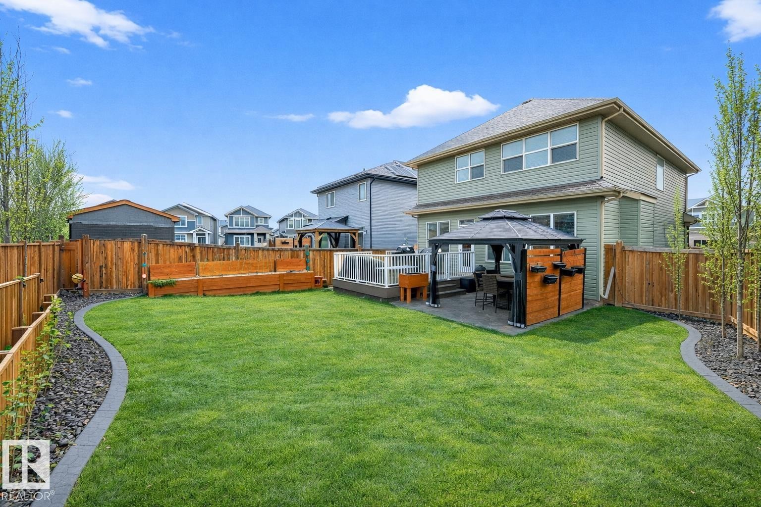 The property features a spacious lawn, a paved patio area with a gazebo, and raised garden beds - 17838 60A Street, Edmonton, AB - Outdoor With Deck Patio Veranda With Backyard