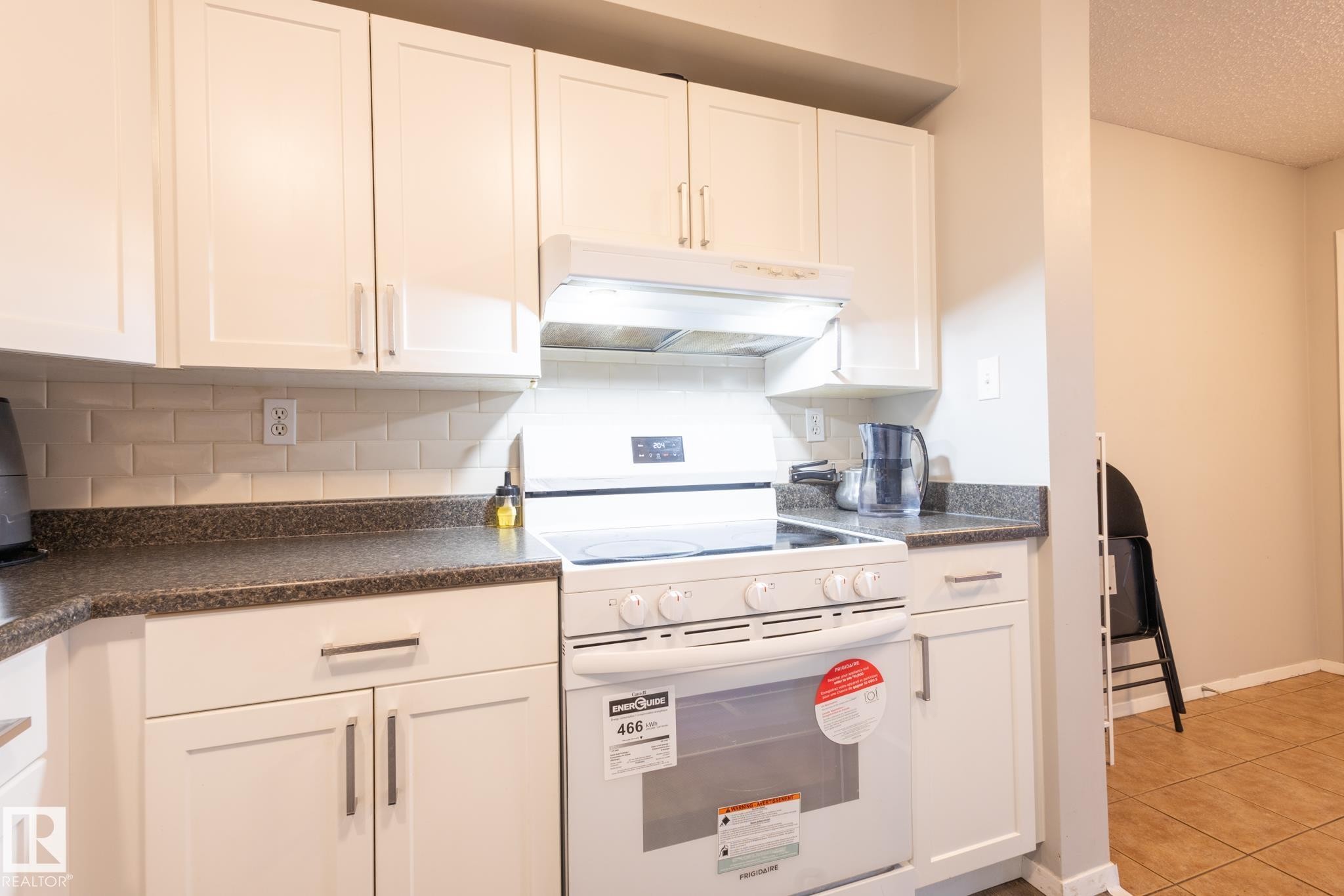 Kitchen featuring white electric range oven, dark countertops, under cabinet range hood, white cabinetry, and a textured ceiling - 3530 42 Street, Edmonton, AB - Indoor Photo Showing Other Room
