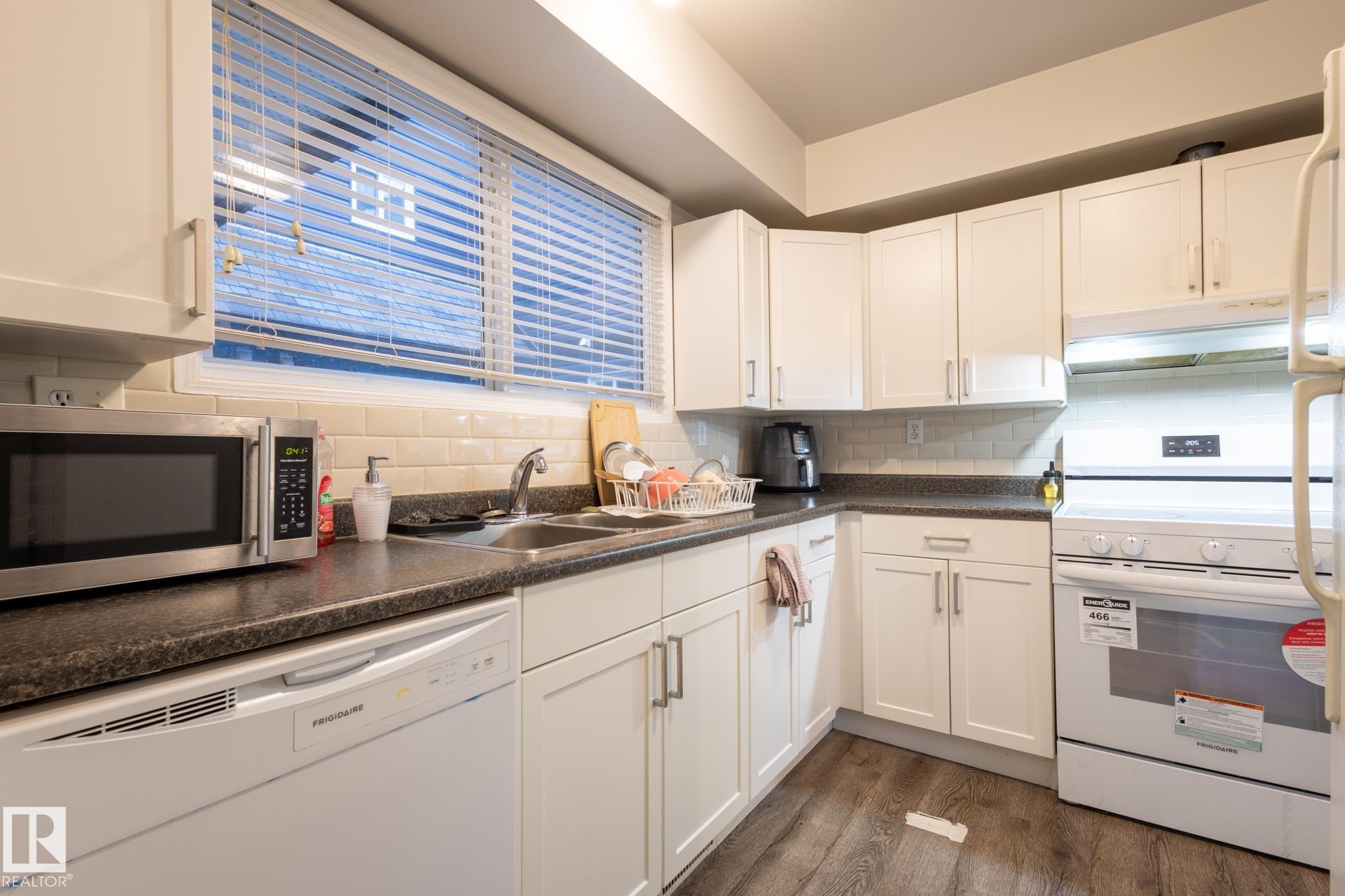 Kitchen with white appliances, dark countertops, dark wood-style flooring, white cabinetry, and decorative backsplash - 3530 42 Street, Edmonton, AB - Indoor Photo Showing Kitchen With Double Sink