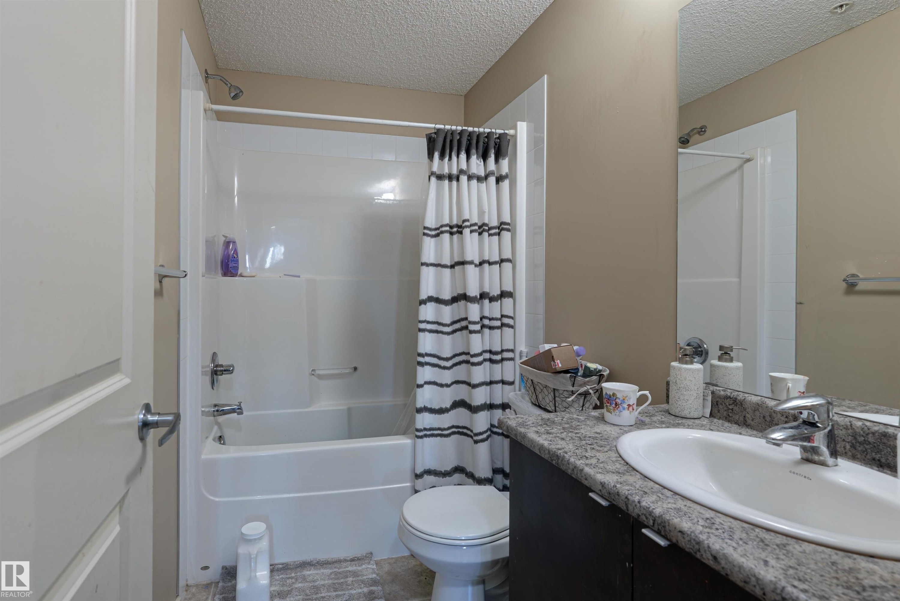 Bathroom featuring a textured ceiling, vanity, and shower / bath combination with curtain - 211 340 Windermere Road, Edmonton, AB - Indoor Photo Showing Bathroom