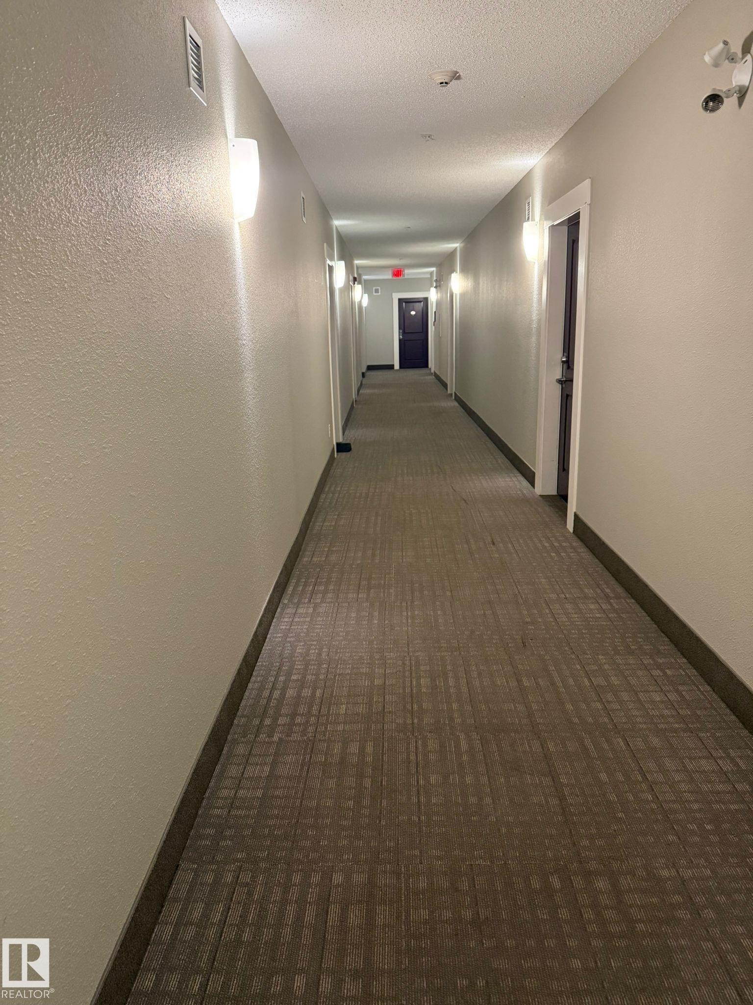 Hall featuring dark carpet, a textured wall, and a textured ceiling - 211 340 Windermere Road, Edmonton, AB - Indoor Photo Showing Other Room