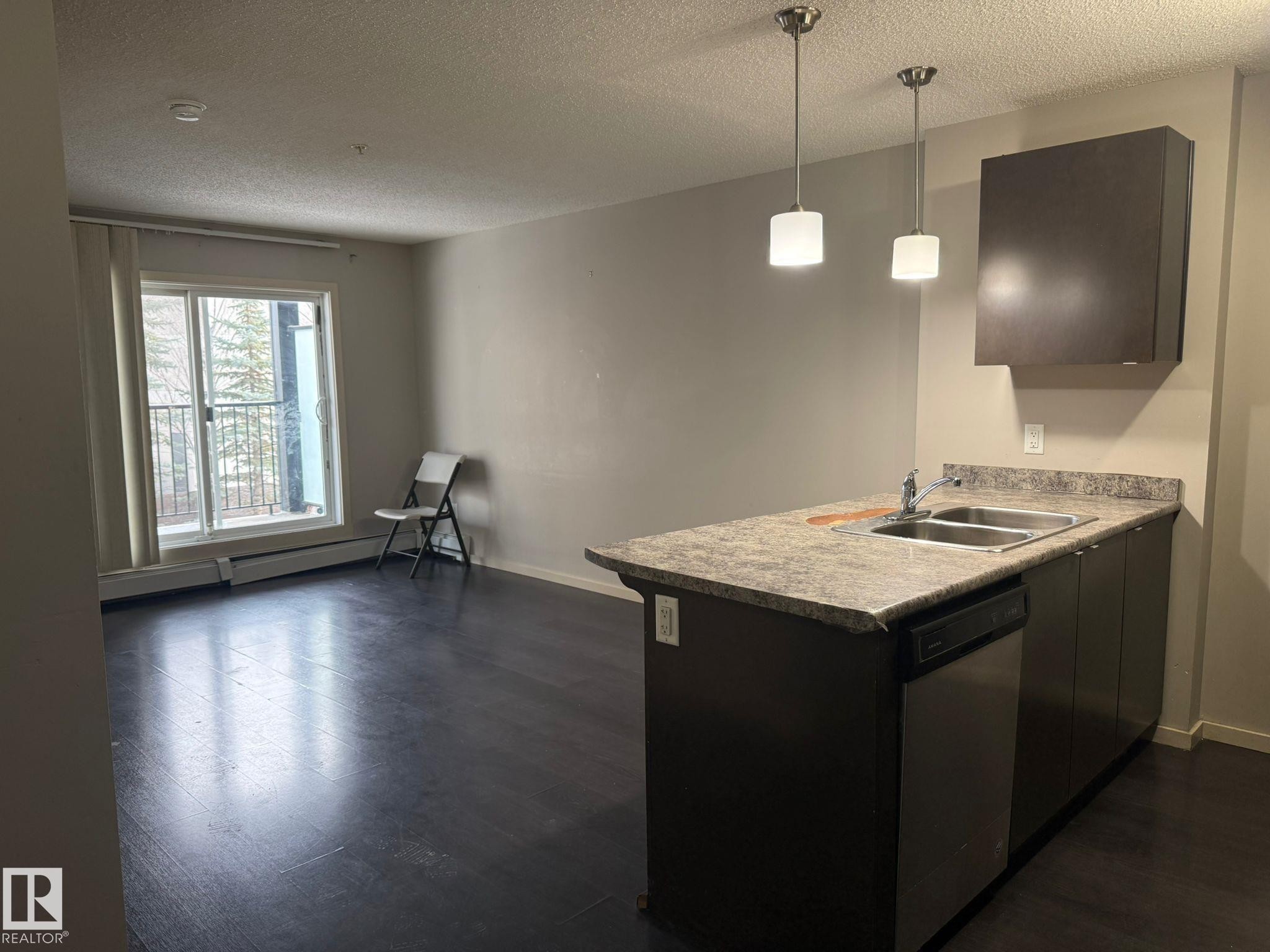 Kitchen with light countertops, dishwasher, a peninsula, hanging light fixtures, and dark wood-style floors - 211 340 Windermere Road, Edmonton, AB - Indoor Photo Showing Kitchen With Double Sink