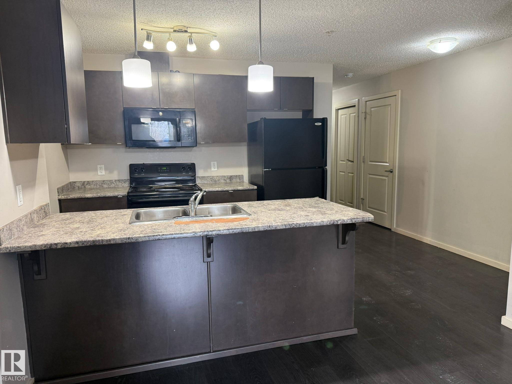 Kitchen featuring black appliances, a peninsula, a textured ceiling, a kitchen breakfast bar, and pendant lighting - 211 340 Windermere Road, Edmonton, AB - Indoor Photo Showing Kitchen With Double Sink With Upgraded Kitchen