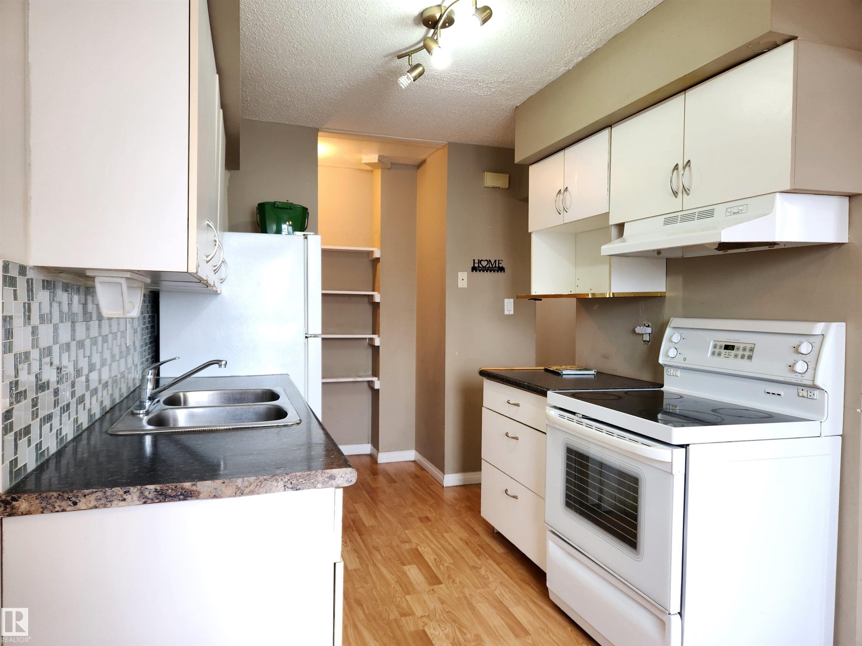 Kitchen featuring electric stove, white cabinetry, freestanding refrigerator, a textured ceiling, and dark countertops - 6 14320 80 Street, Edmonton, AB - Indoor Photo Showing Kitchen With Double Sink