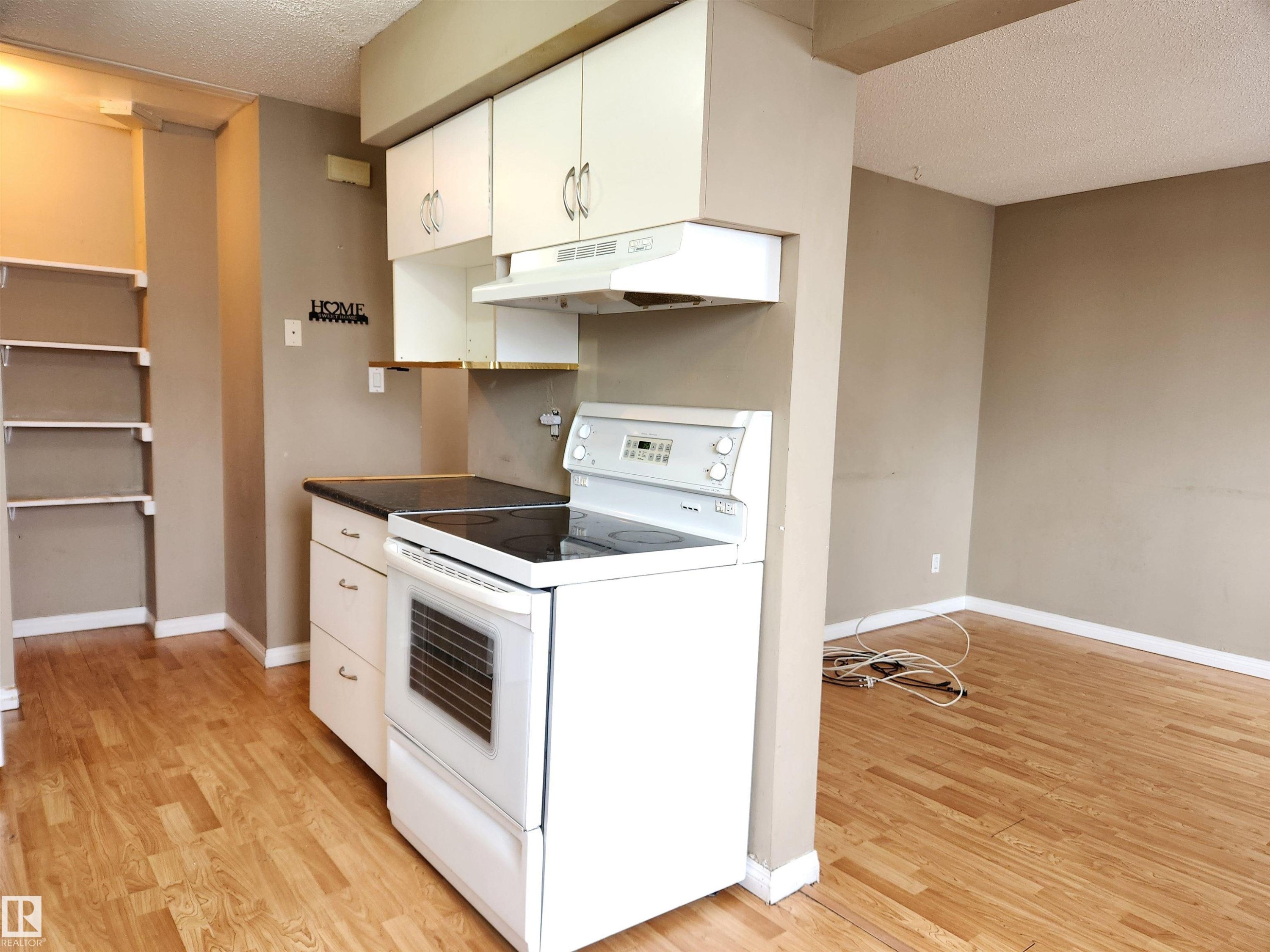 Kitchen featuring electric stove, a textured ceiling, white cabinetry, dark countertops, and light wood finished floors - 6 14320 80 Street, Edmonton, AB - Indoor Photo Showing Kitchen