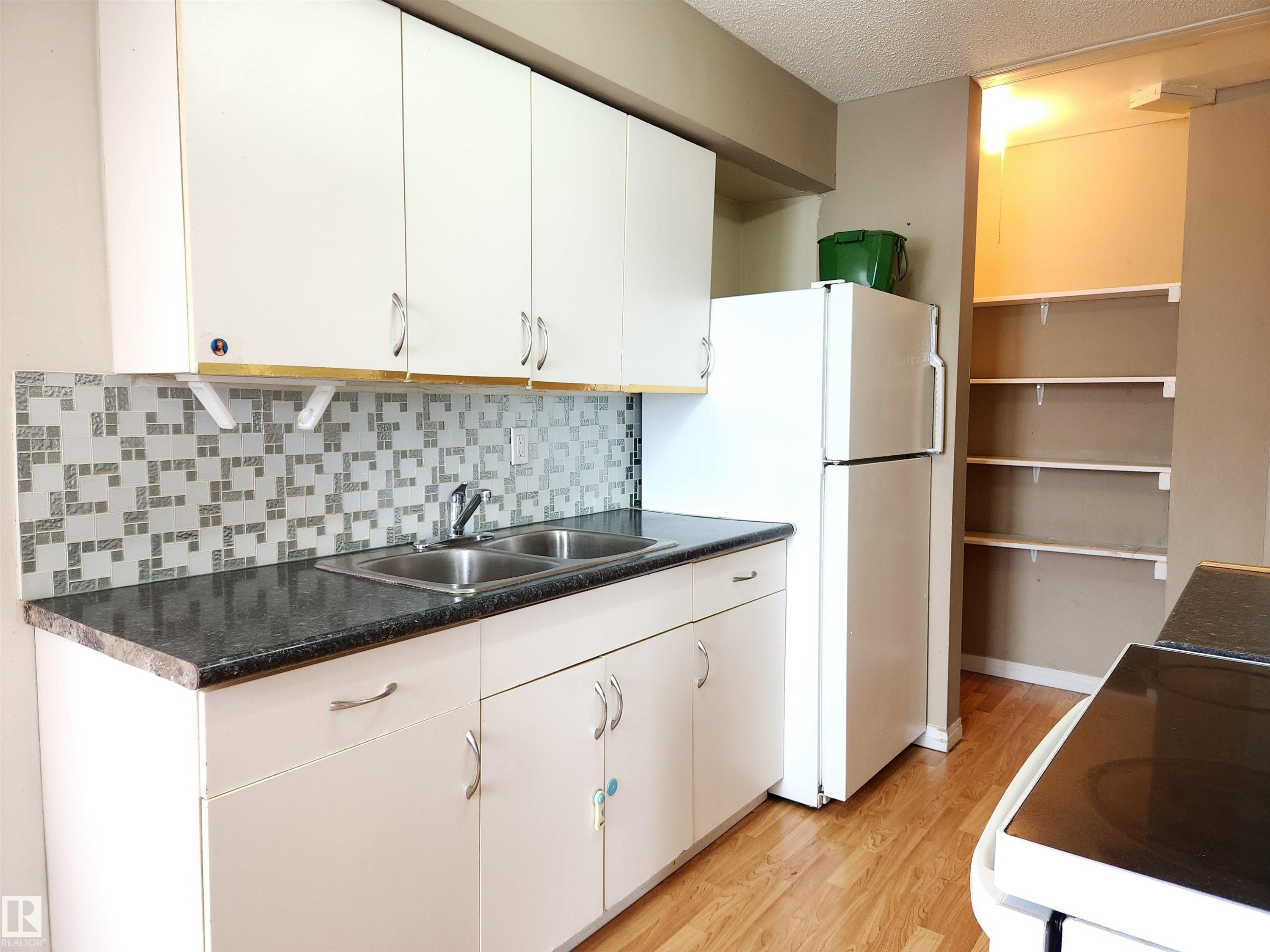 Kitchen featuring white cabinetry, black electric range, light wood finished floors, dark countertops, and freestanding refrigerator - 6 14320 80 Street, Edmonton, AB - Indoor Photo Showing Kitchen With Double Sink
