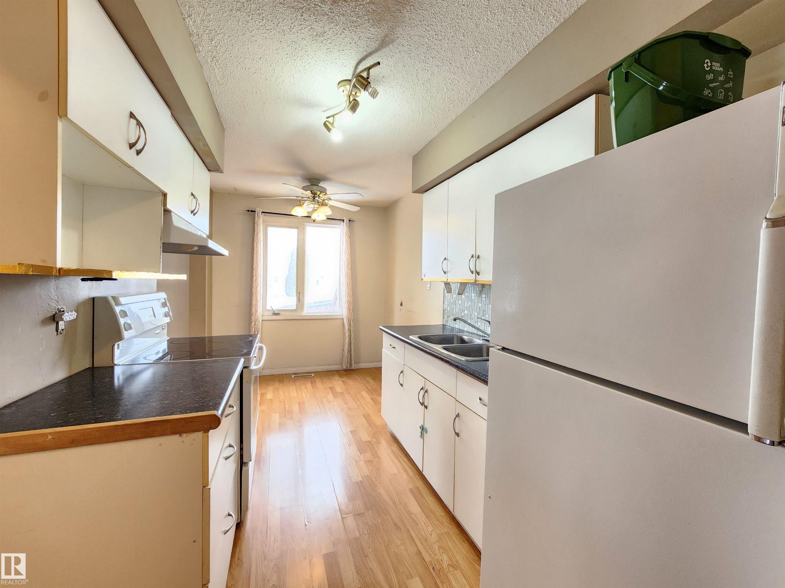 Kitchen featuring white appliances, dark countertops, a ceiling fan, a textured ceiling, and light wood-style floors - 6 14320 80 Street, Edmonton, AB - Indoor Photo Showing Kitchen With Double Sink