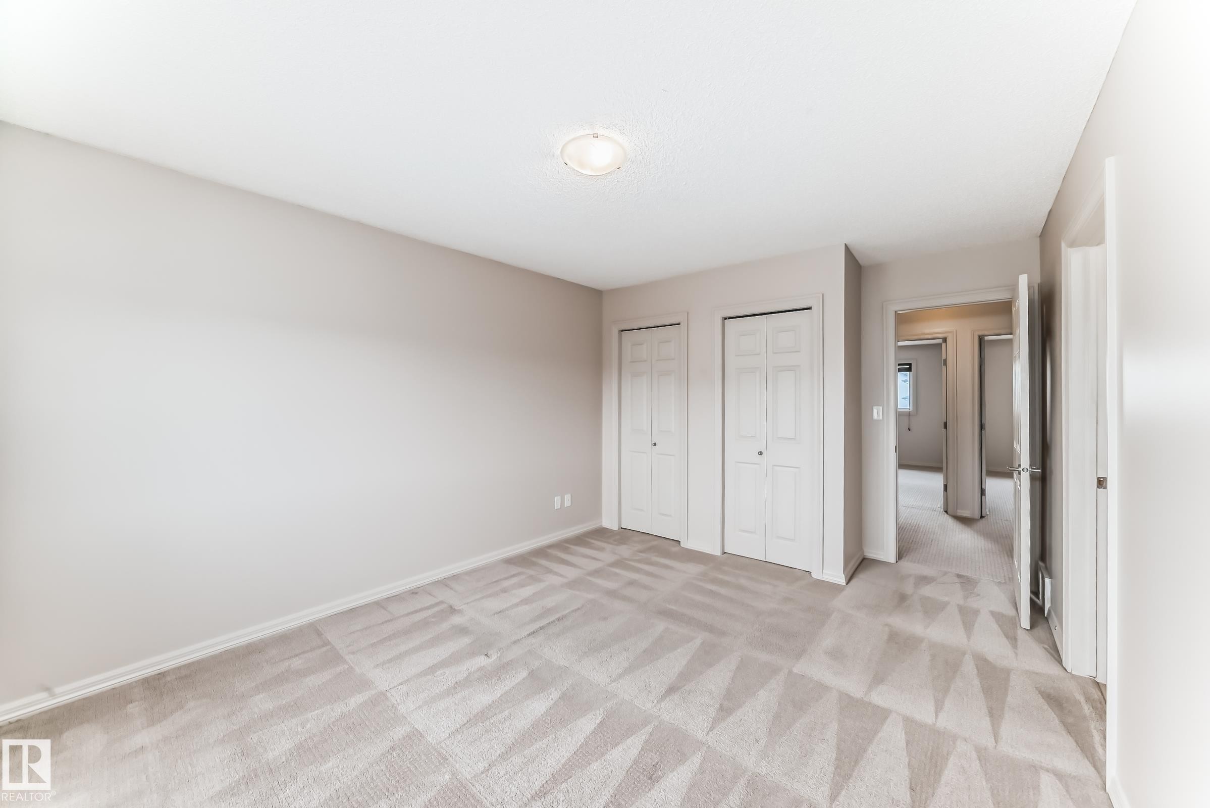 Spacious interior room featuring light-toned walls, patterned carpeting, and white bi-fold closet doors - 1285 Cunningham Drive, Edmonton, AB - Indoor Photo Showing Other Room