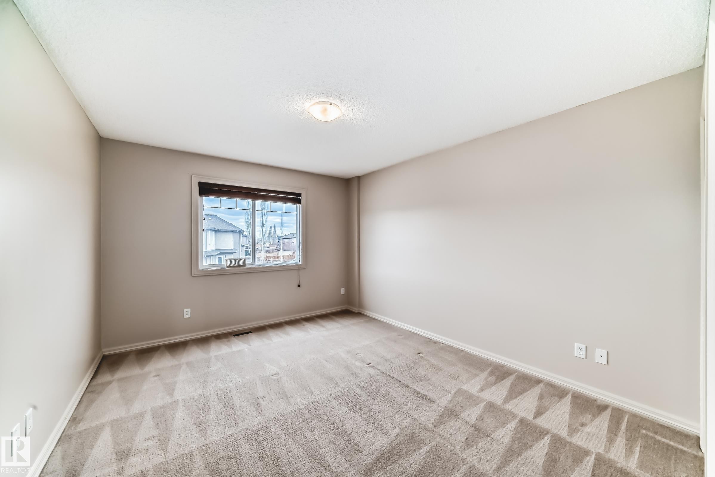 Spacious interior room featuring light gray walls, patterned carpeting, and a single window with dark wood-finish blinds - 1285 Cunningham Drive, Edmonton, AB - Indoor Photo Showing Other Room