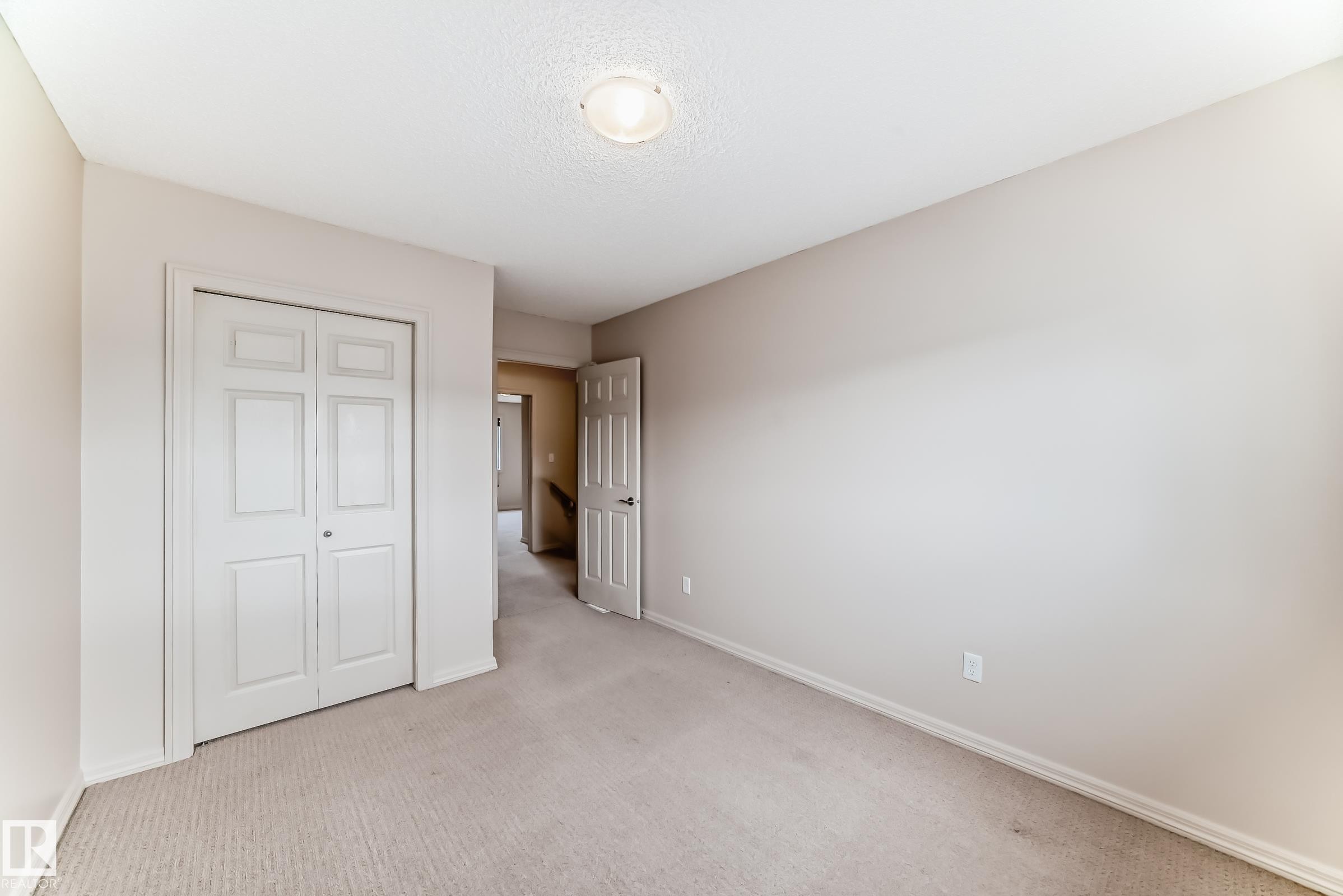 Neutral-toned bedroom featuring carpeted flooring, a bi-fold closet door, and a flush-mount ceiling light fixture - 1285 Cunningham Drive, Edmonton, AB - Indoor Photo Showing Other Room