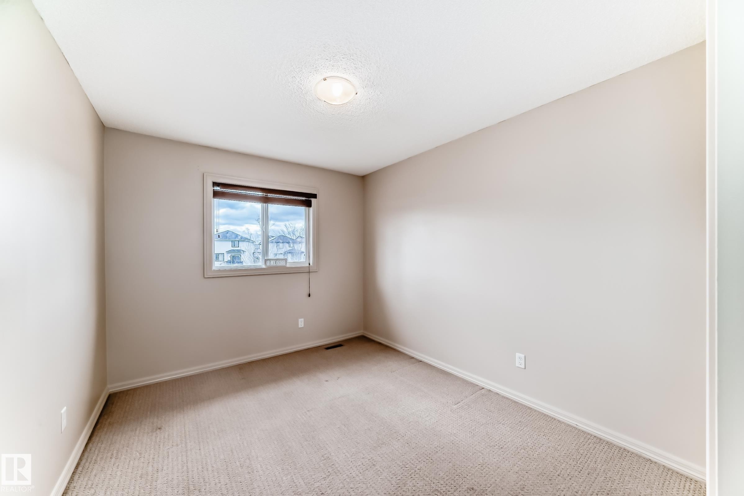 Neutral-toned room featuring a single window with blinds, light-colored carpeting, white baseboards, and a ceiling-mounted light fixture - 1285 Cunningham Drive, Edmonton, AB - Indoor Photo Showing Other Room