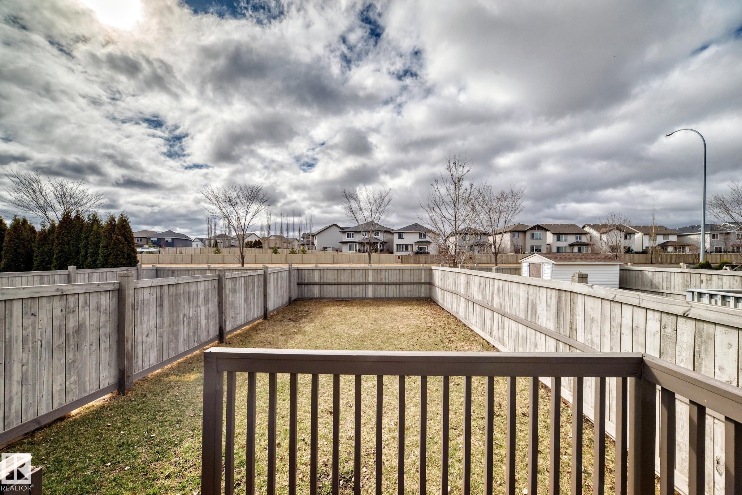 Fenced backyard with a wooden privacy fence, a wooden deck railing, and a grass area - 1285 Cunningham Drive, Edmonton, AB - Outdoor