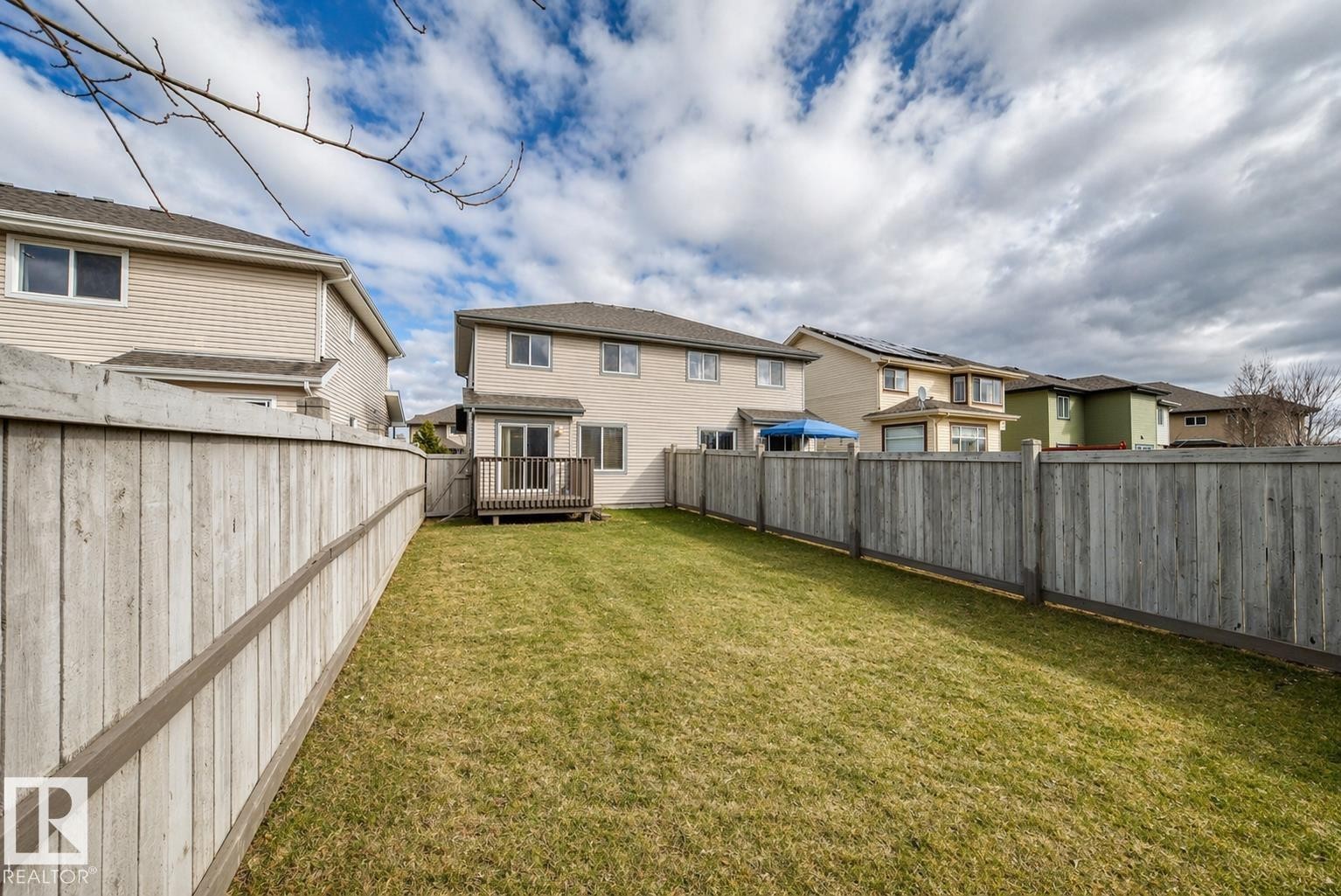 Expansive backyard featuring a manicured lawn, full perimeter privacy fencing, and a ground-level deck with sliding door access to the residence - 1285 Cunningham Drive, Edmonton, AB - Outdoor With Exterior