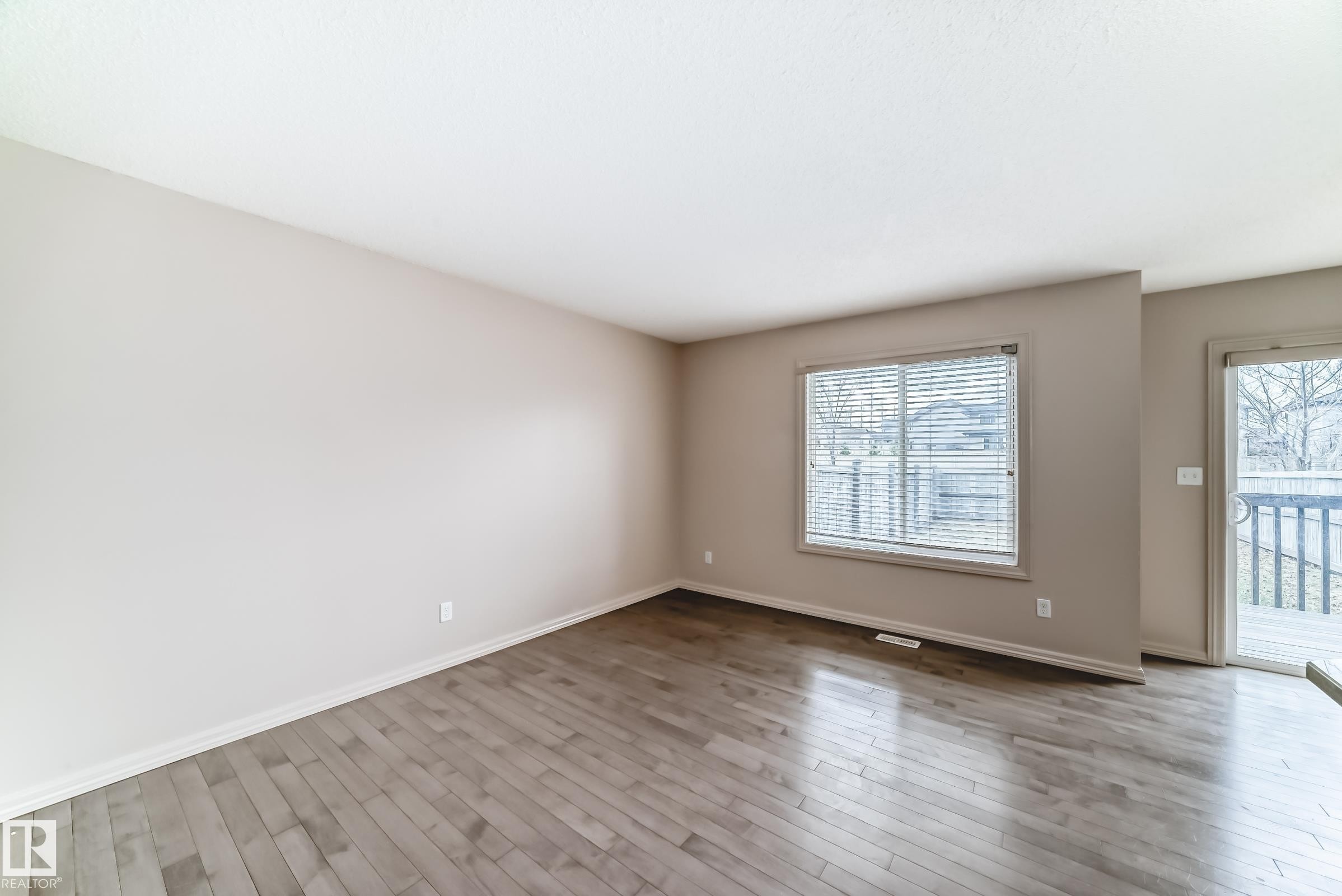 Spacious room featuring wood-finish flooring, a large window with horizontal blinds, and a sliding glass door providing exterior access to a deck - 1285 Cunningham Drive, Edmonton, AB - Indoor Photo Showing Other Room