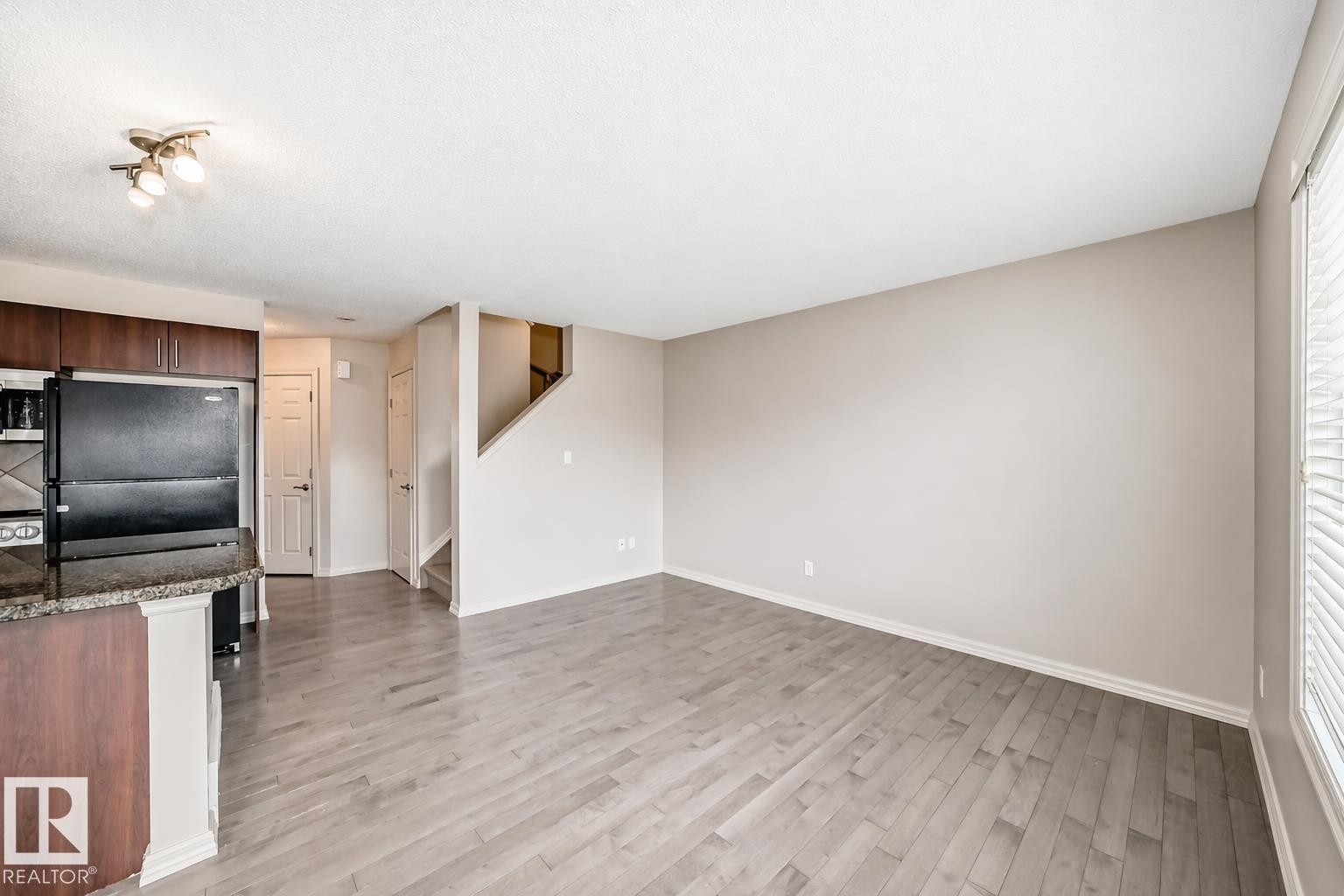 Open-concept living area featuring light wood-finish flooring, neutral wall tones, and a large window with horizontal blinds - 1285 Cunningham Drive, Edmonton, AB - Indoor