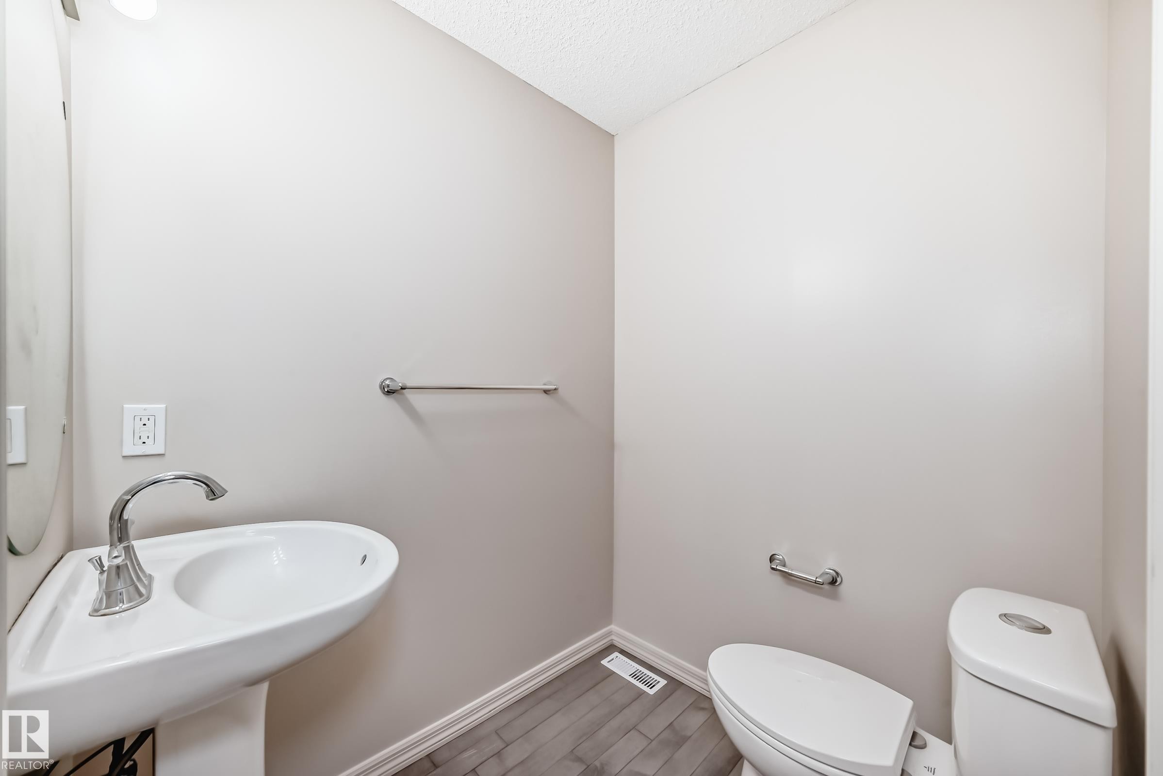 Pedestal sink and toilet in a light-toned powder room, featuring wood-finish flooring and a chrome towel bar - 1285 Cunningham Drive, Edmonton, AB - Indoor Photo Showing Bathroom
