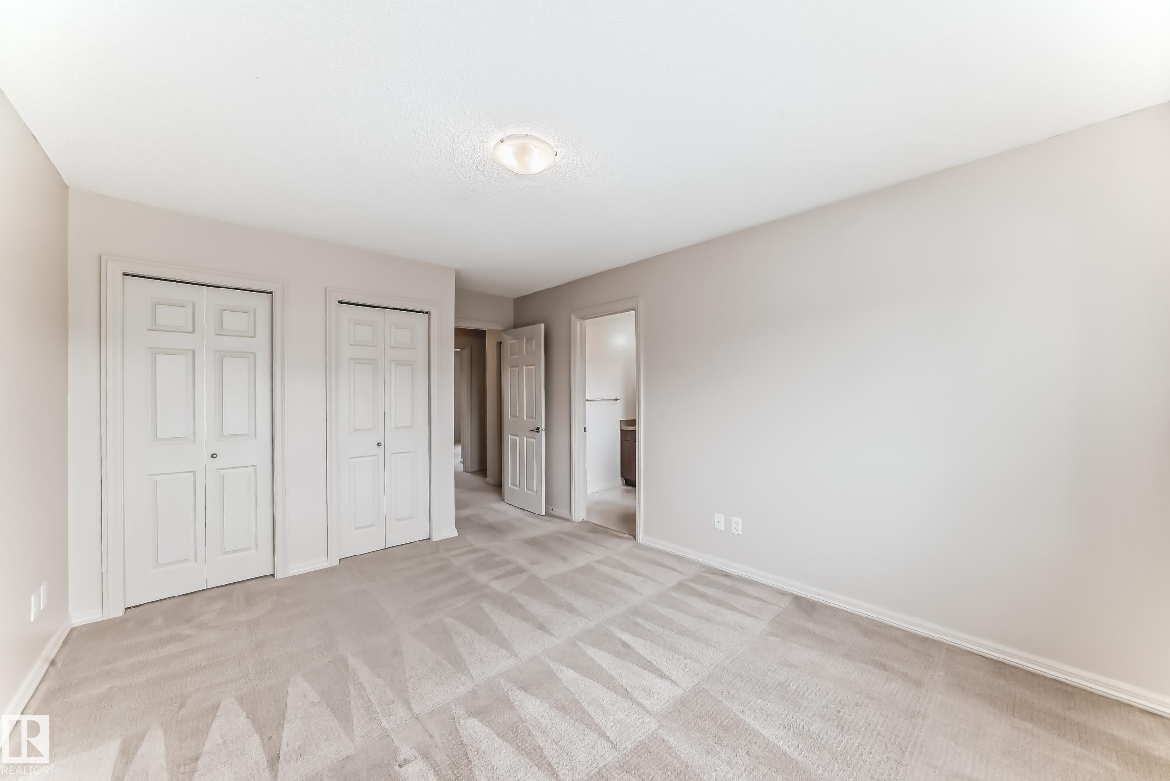 Carpeted room featuring two bifold door closets, light neutral wall paint, white baseboards, and a flush mount ceiling light fixture - 1285 Cunningham Drive, Edmonton, AB - Indoor Photo Showing Other Room