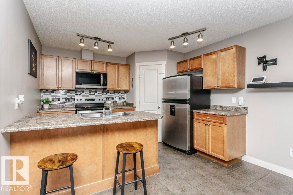 Kitchen with a kitchen bar, stainless steel appliances, rail lighting, decorative backsplash, and a peninsula - 1381 Rutherford Road, Edmonton, AB - Indoor Photo Showing Kitchen With Stainless Steel Kitchen With Double Sink