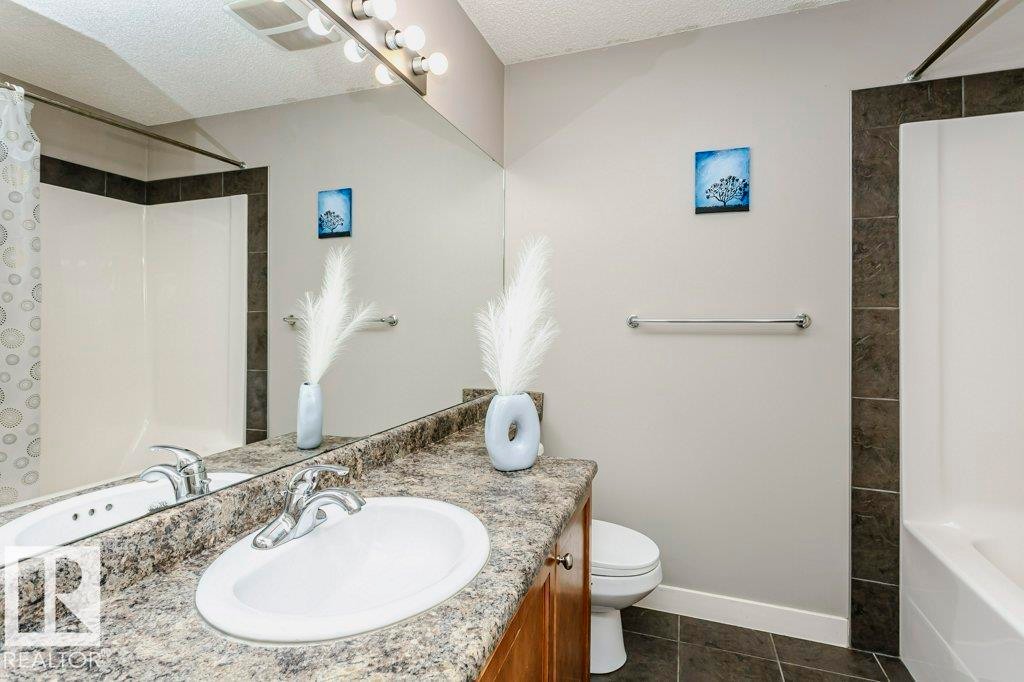 Bathroom featuring vanity, shower / tub combo, a textured ceiling, and dark tile patterned flooring - 1381 Rutherford Road, Edmonton, AB - Indoor Photo Showing Bathroom