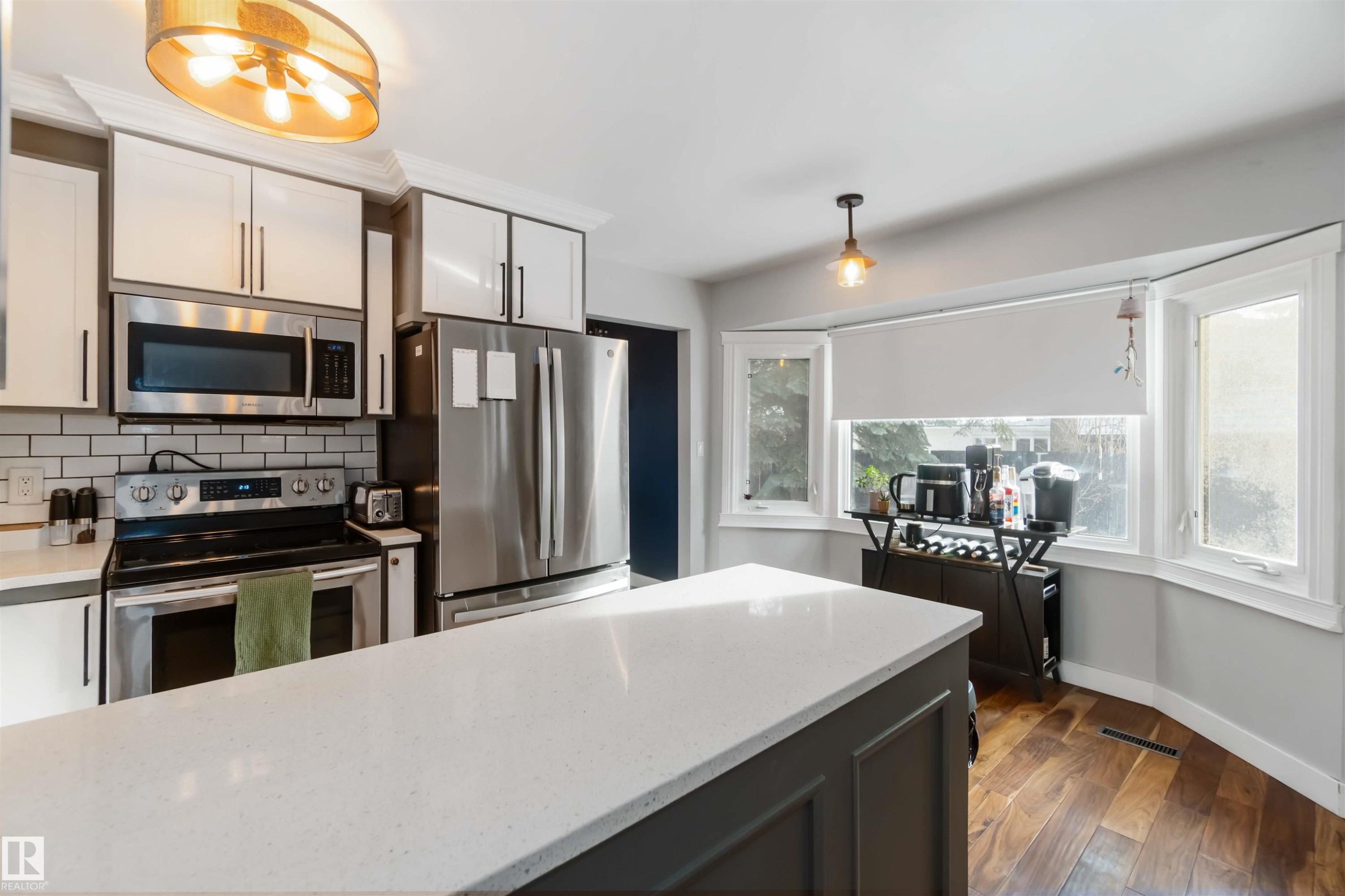 Kitchen featuring stainless steel appliances, light stone counters, dark wood-style floors, backsplash, and hanging light fixtures - 6 Garraway Pl, St. Albert, AB - Indoor Photo Showing Kitchen