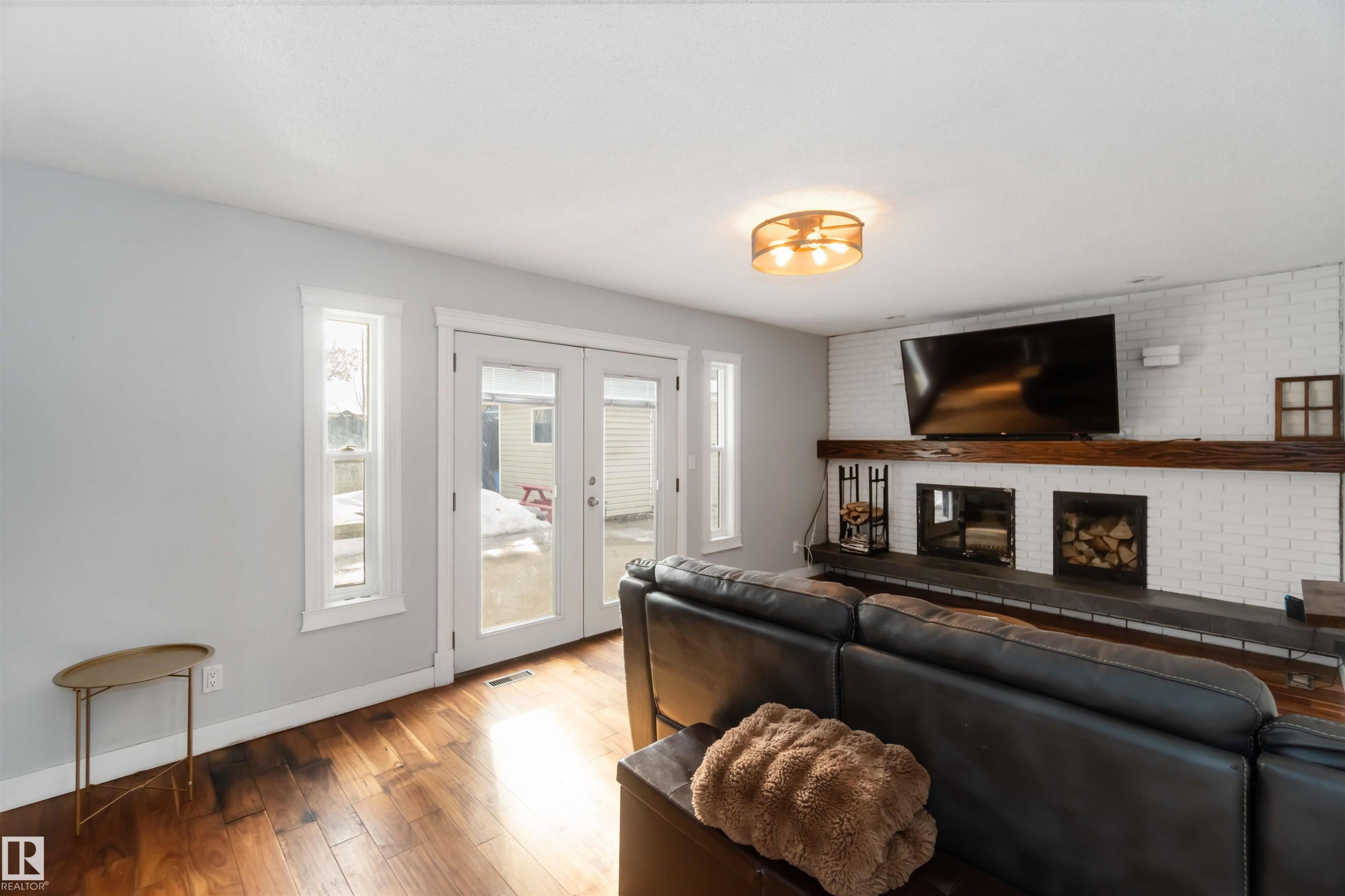 Living area featuring wood finished floors, healthy amount of natural light, french doors, brick wall, and a fireplace - 6 Garraway Pl, St. Albert, AB - Indoor Photo Showing Living Room With Fireplace