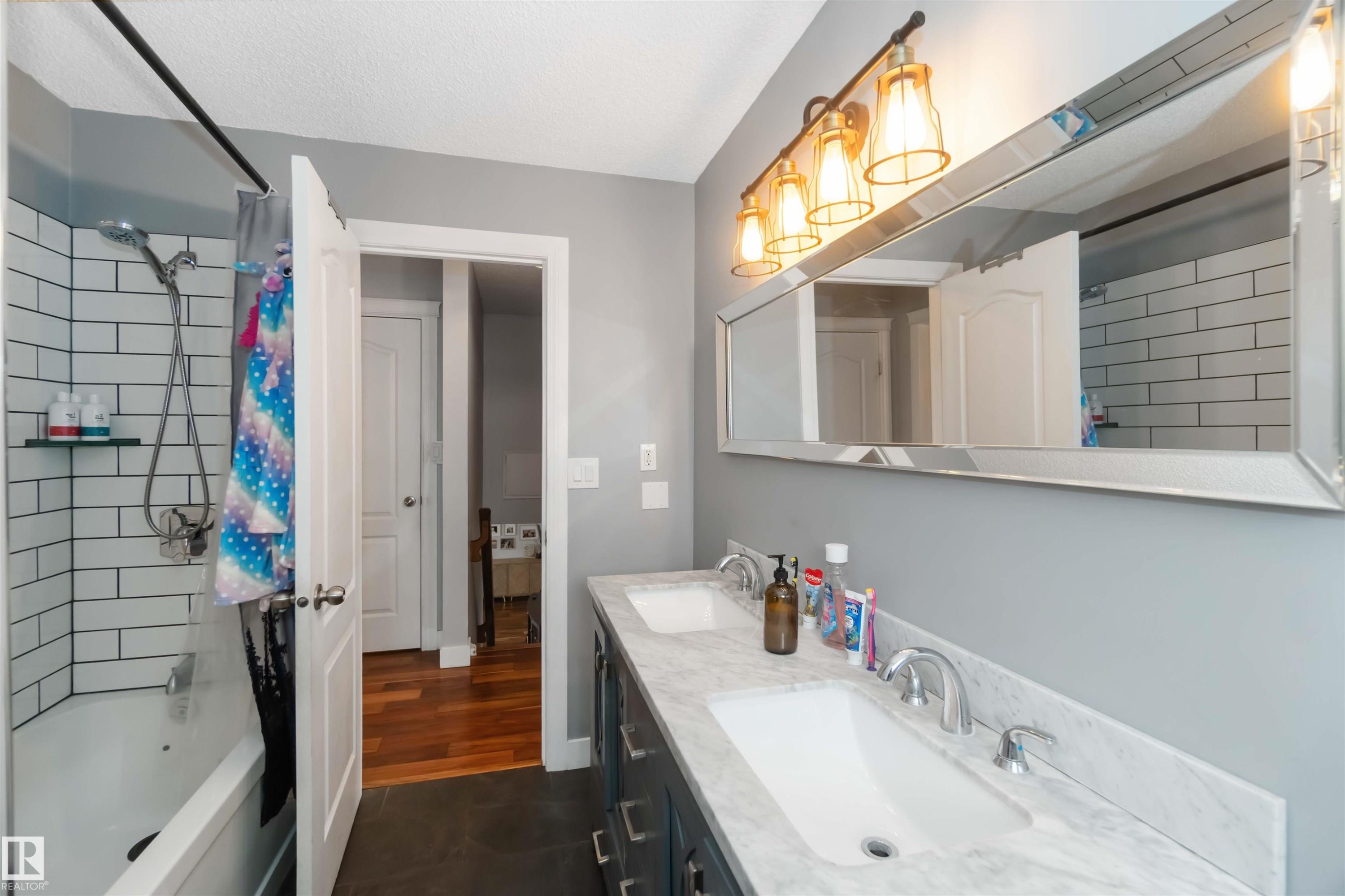Bathroom featuring shower / bath combination with curtain, double vanity, dark tile patterned flooring, and a textured ceiling - 6 Garraway Pl, St. Albert, AB - Indoor Photo Showing Bathroom