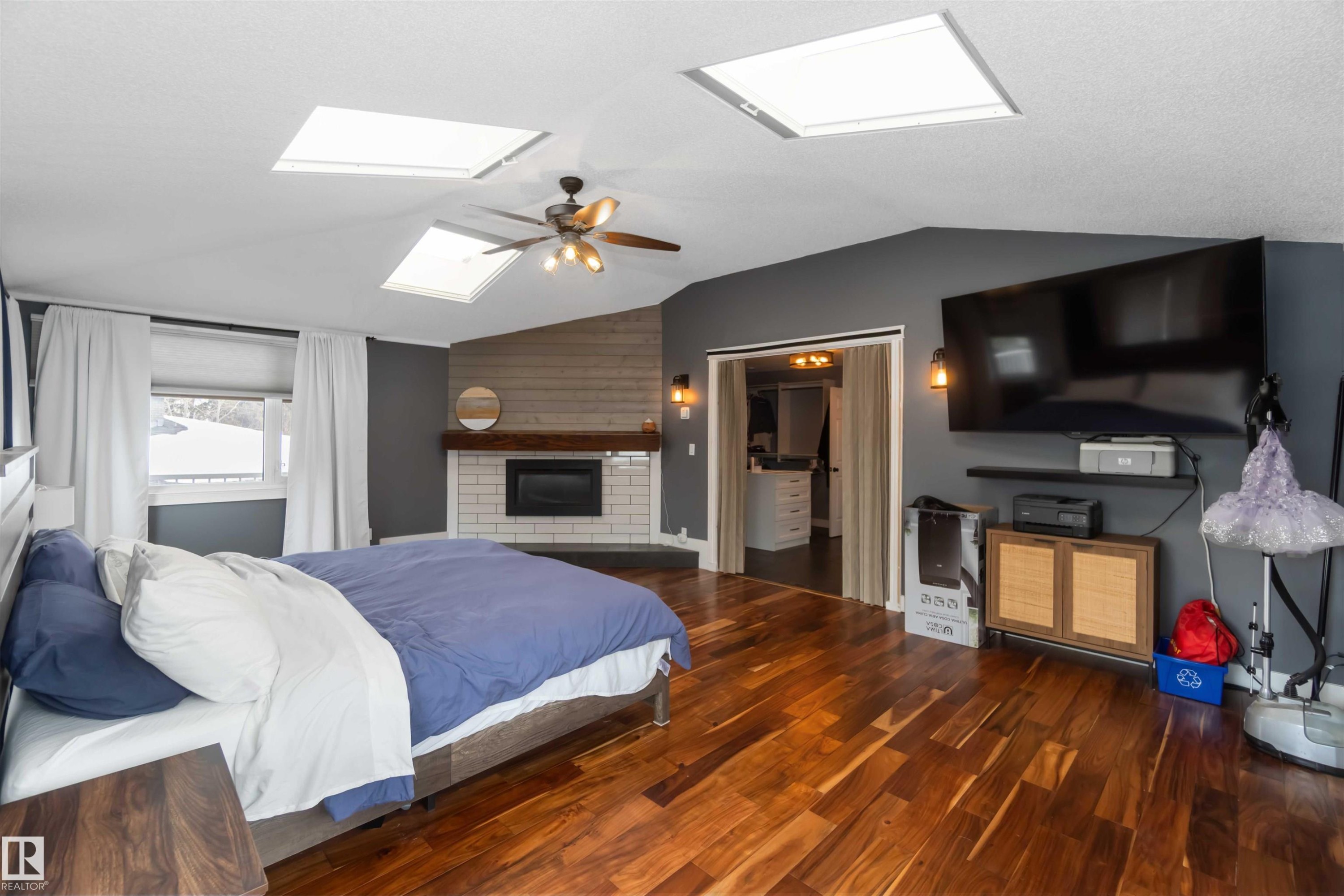Bedroom with dark wood-style floors, ceiling fan, a skylight, and a fireplace - 6 Garraway Pl, St. Albert, AB - Indoor Photo Showing Bedroom