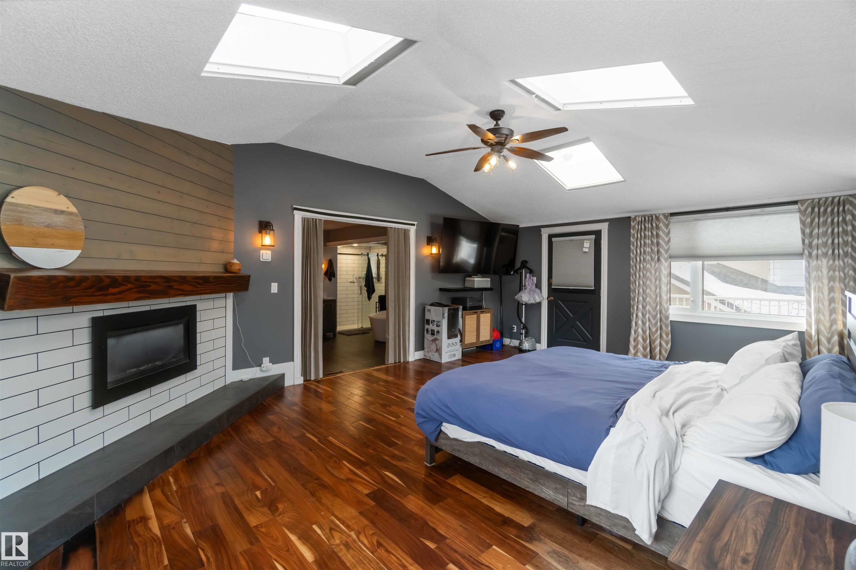 Bedroom featuring wood finished floors, a skylight, lofted ceiling, a ceiling fan, and a fireplace - 6 Garraway Pl, St. Albert, AB - Indoor Photo Showing Bedroom With Fireplace