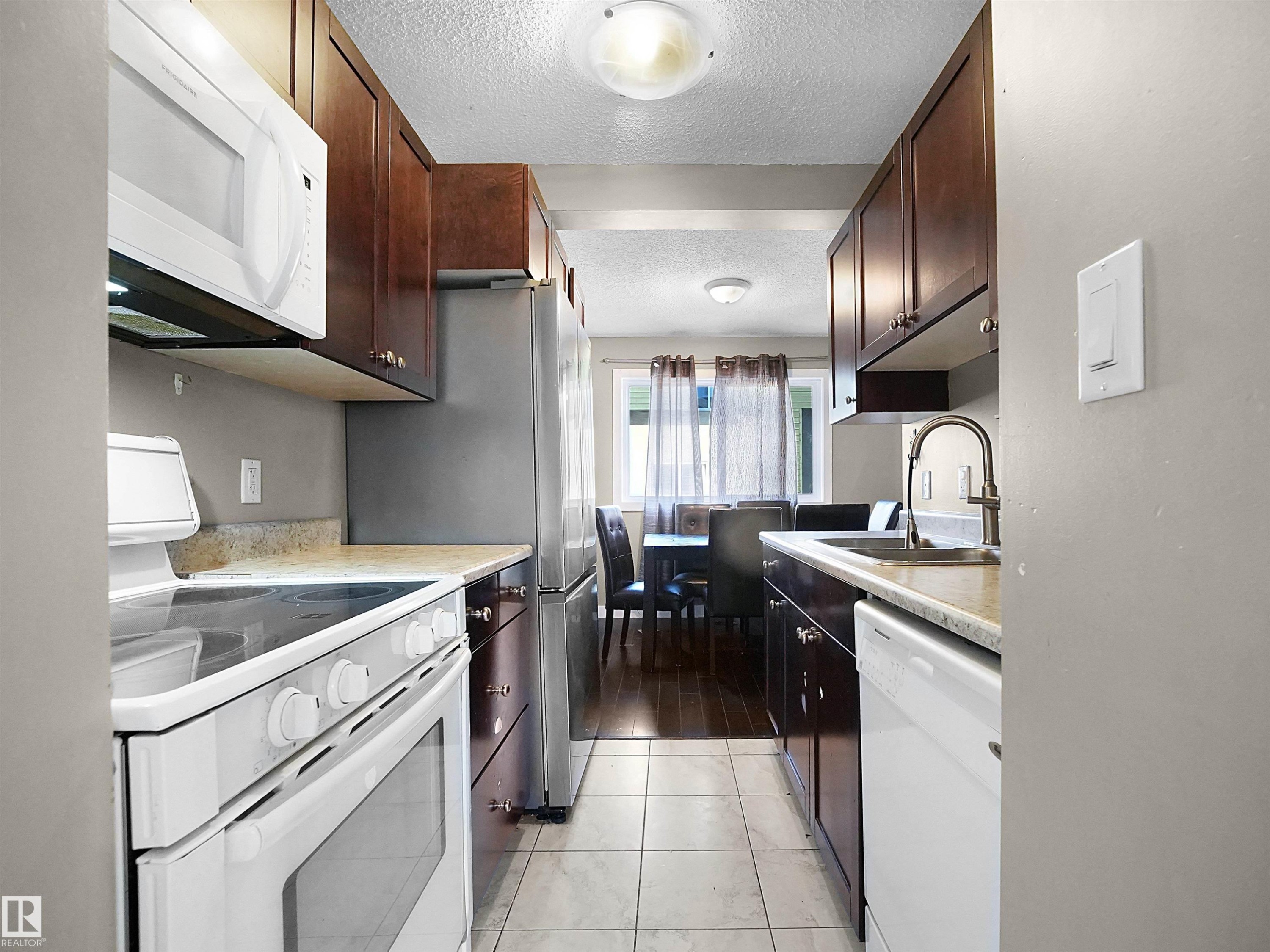 Kitchen featuring white appliances, light countertops, a textured ceiling, dark brown cabinetry, and light tile patterned flooring - 791 Abbottsfield Road, Edmonton, AB - Indoor Photo Showing Kitchen With Upgraded Kitchen