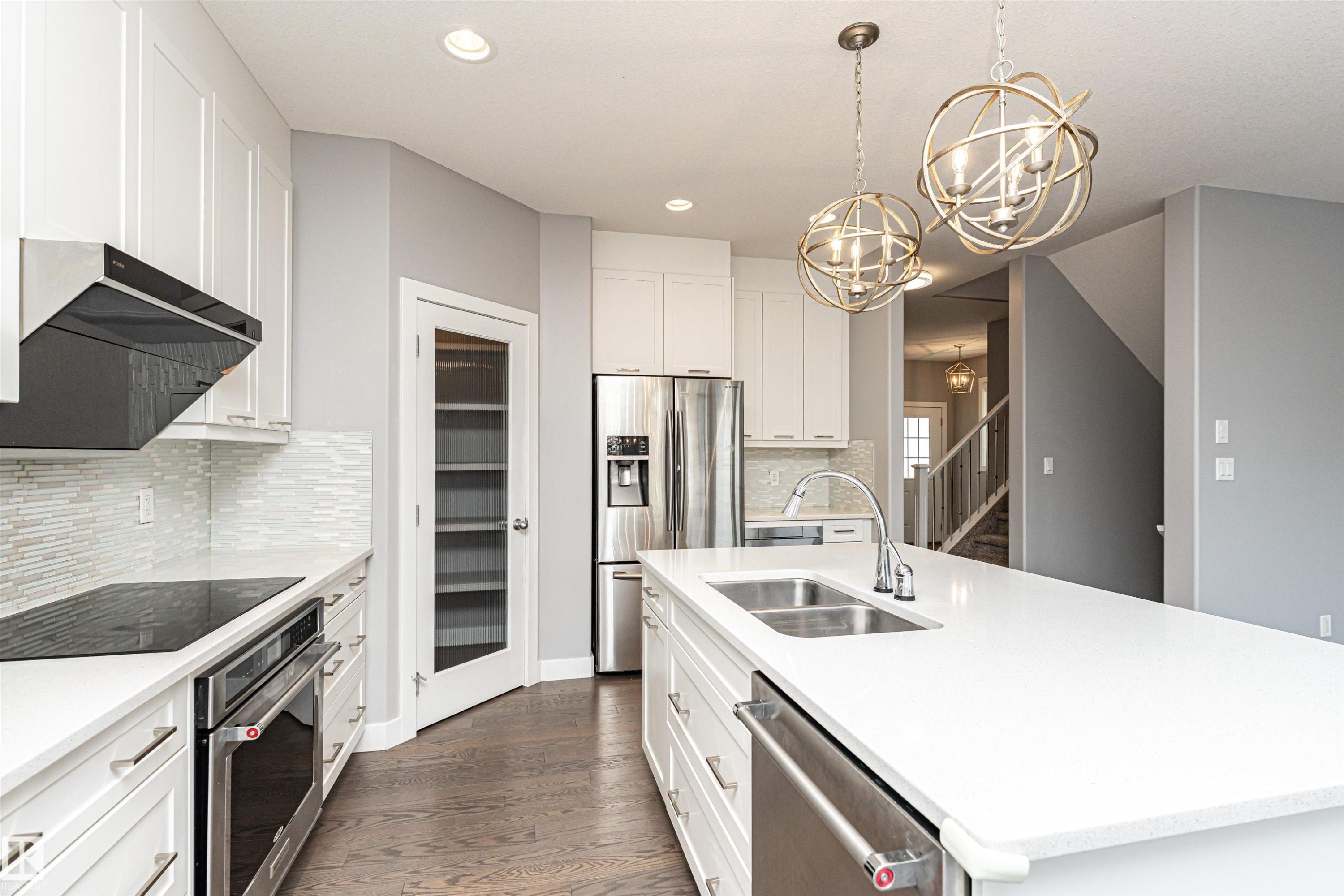 Kitchen featuring white cabinets, a center island with sink, stainless steel appliances, a chandelier, and light stone counters - 3611 Keswick Boulevard, Edmonton, AB - Indoor Photo Showing Kitchen With Double Sink With Upgraded Kitchen