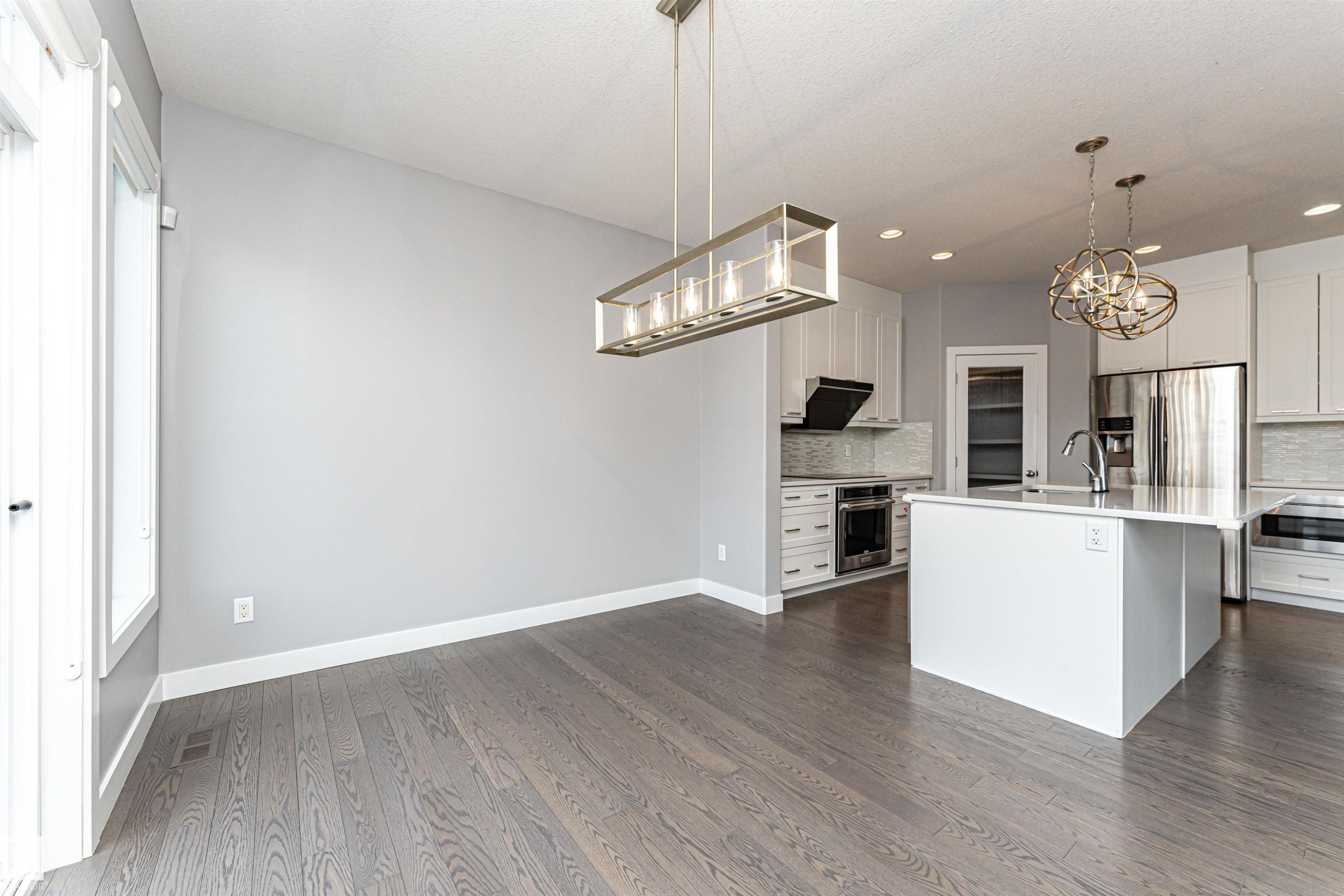 Kitchen featuring suspended lighting, white cabinets, a center island with sink, stainless steel appliances, and dark wood-style floors - 3611 Keswick Boulevard, Edmonton, AB - Indoor Photo Showing Kitchen