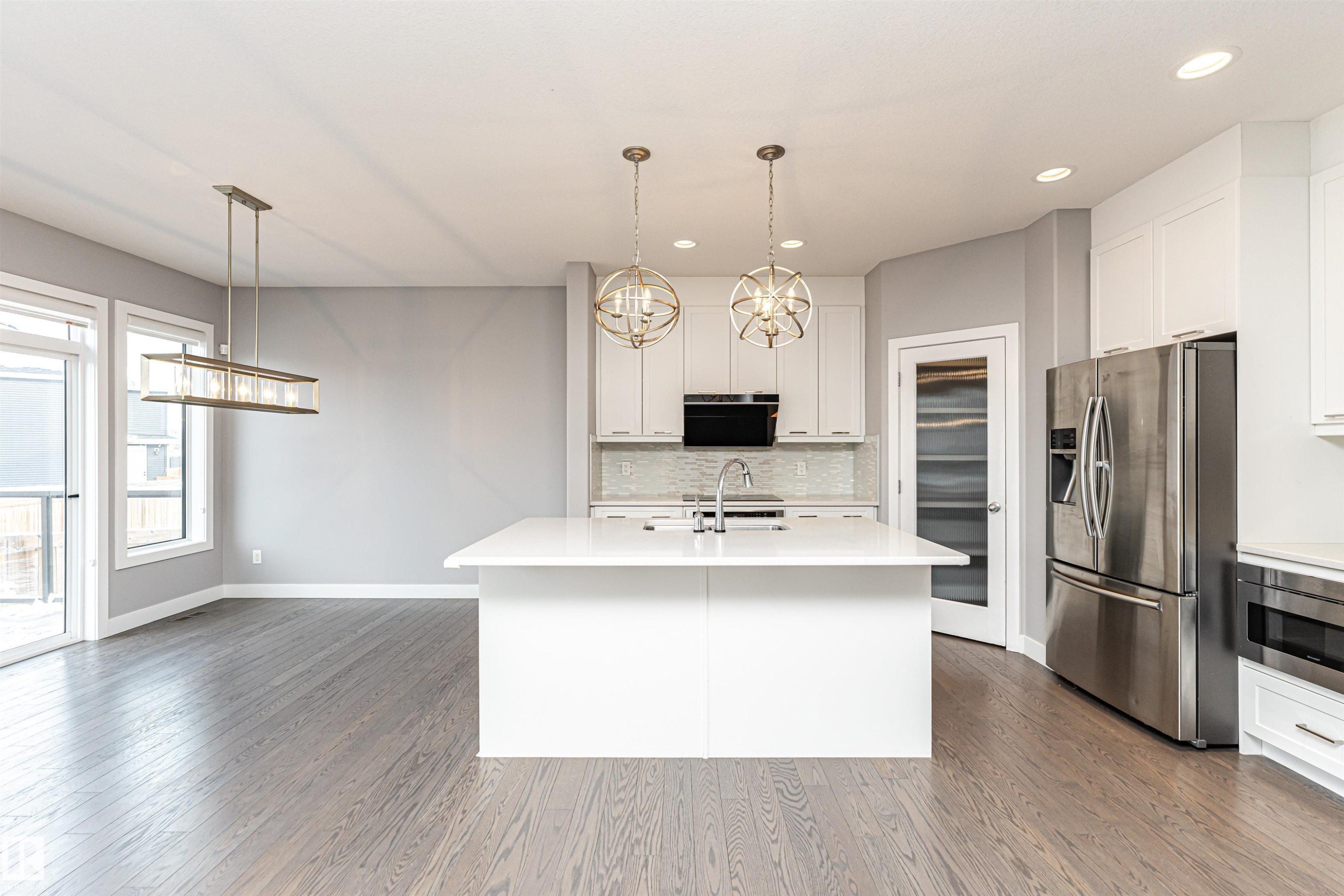 Kitchen featuring white cabinetry, stainless steel appliances, decorative backsplash, a center island with sink, and decorative light fixtures - 3611 Keswick Boulevard, Edmonton, AB - Indoor Photo Showing Kitchen With Upgraded Kitchen