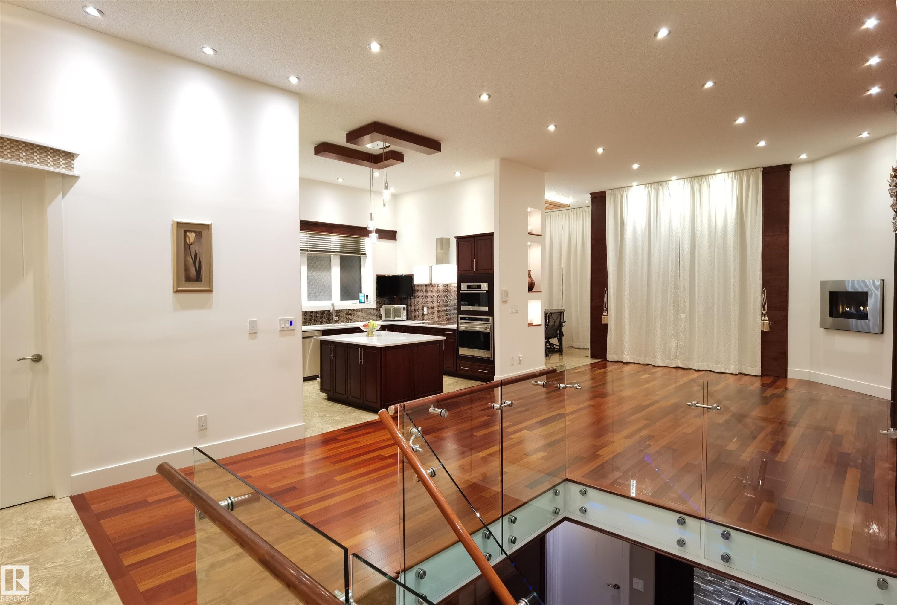 Kitchen featuring dark wood finish cabinetry, decorative backsplash, a kitchen island, stainless steel double oven, and a fireplace - 169 Callaghan Drive, Edmonton, AB - Indoor Photo Showing Other Room