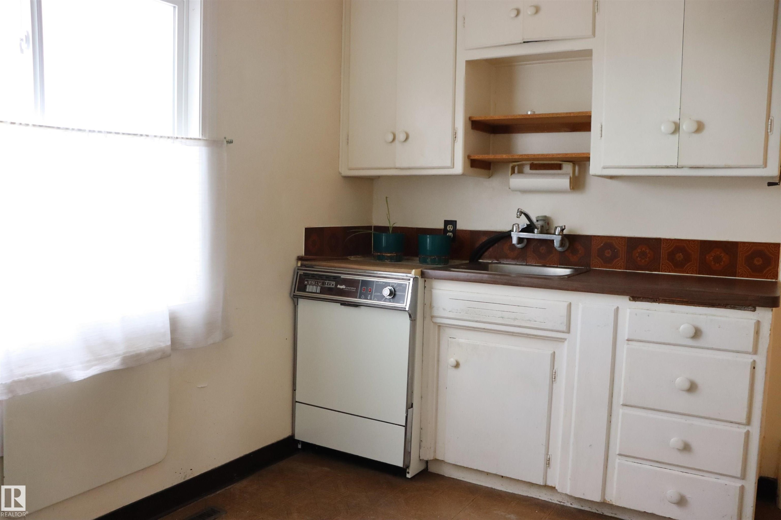 Kitchen with dark countertops, white dishwasher, open shelves, and white cabinets - 11250 72 Avenue, Edmonton, AB