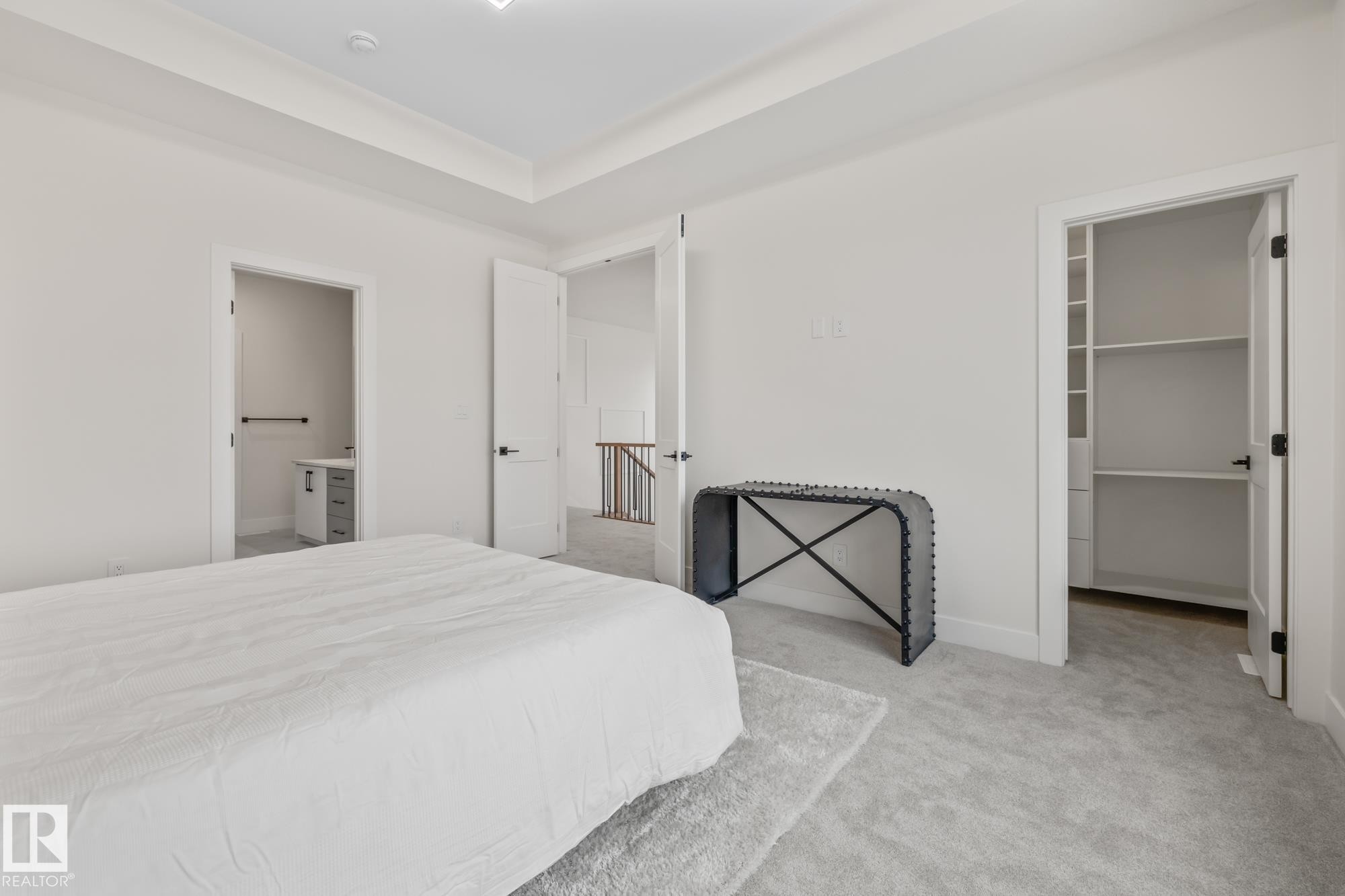 Bedroom featuring a spacious closet, light colored carpet, ensuite bath, and a raised ceiling - 132 Edgewater Circle, Leduc, AB - Indoor Photo Showing Bedroom