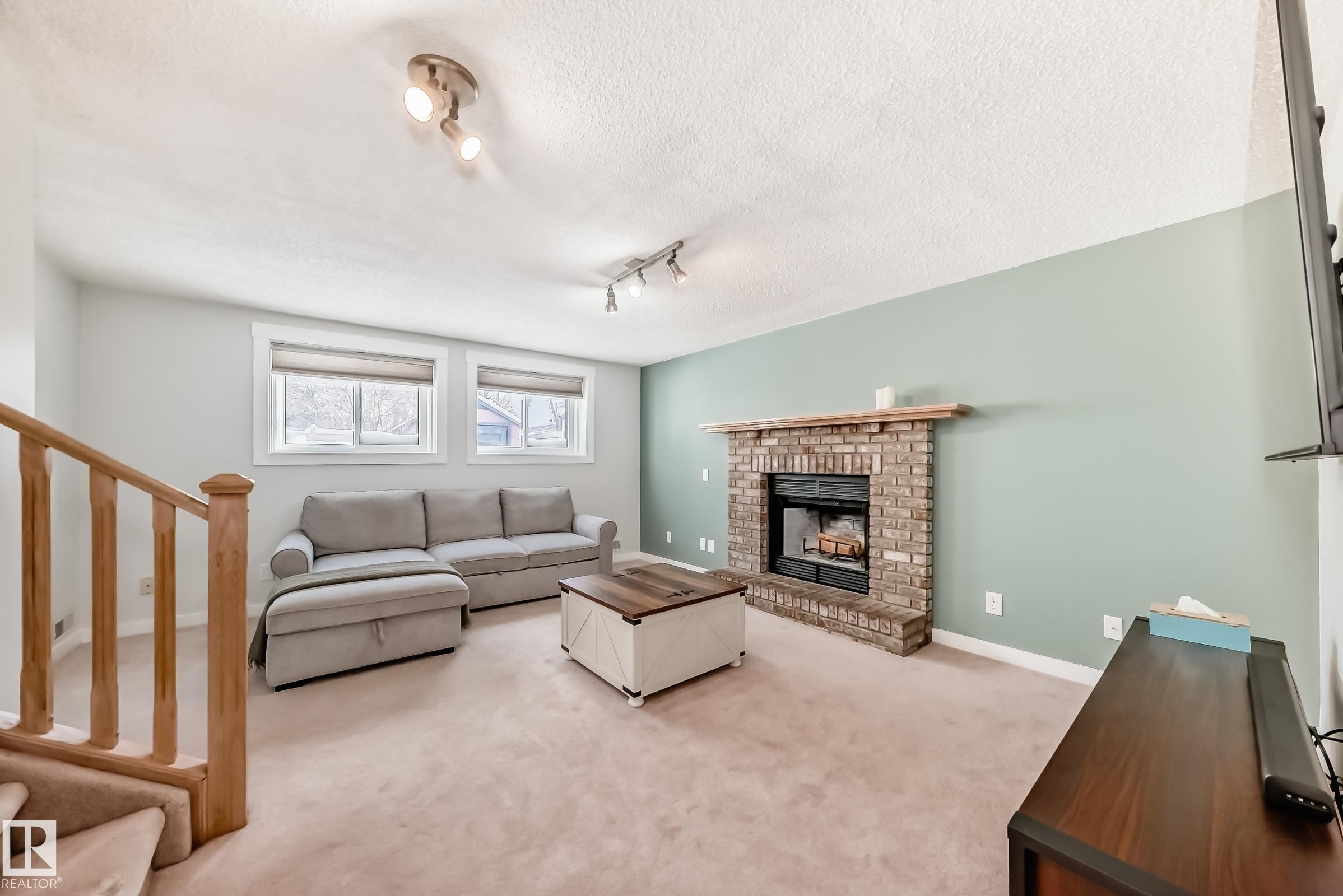 Carpeted living room with a fireplace, rail lighting, and a textured ceiling - 7011 190B Street, Edmonton, AB - Indoor Photo Showing Living Room With Fireplace