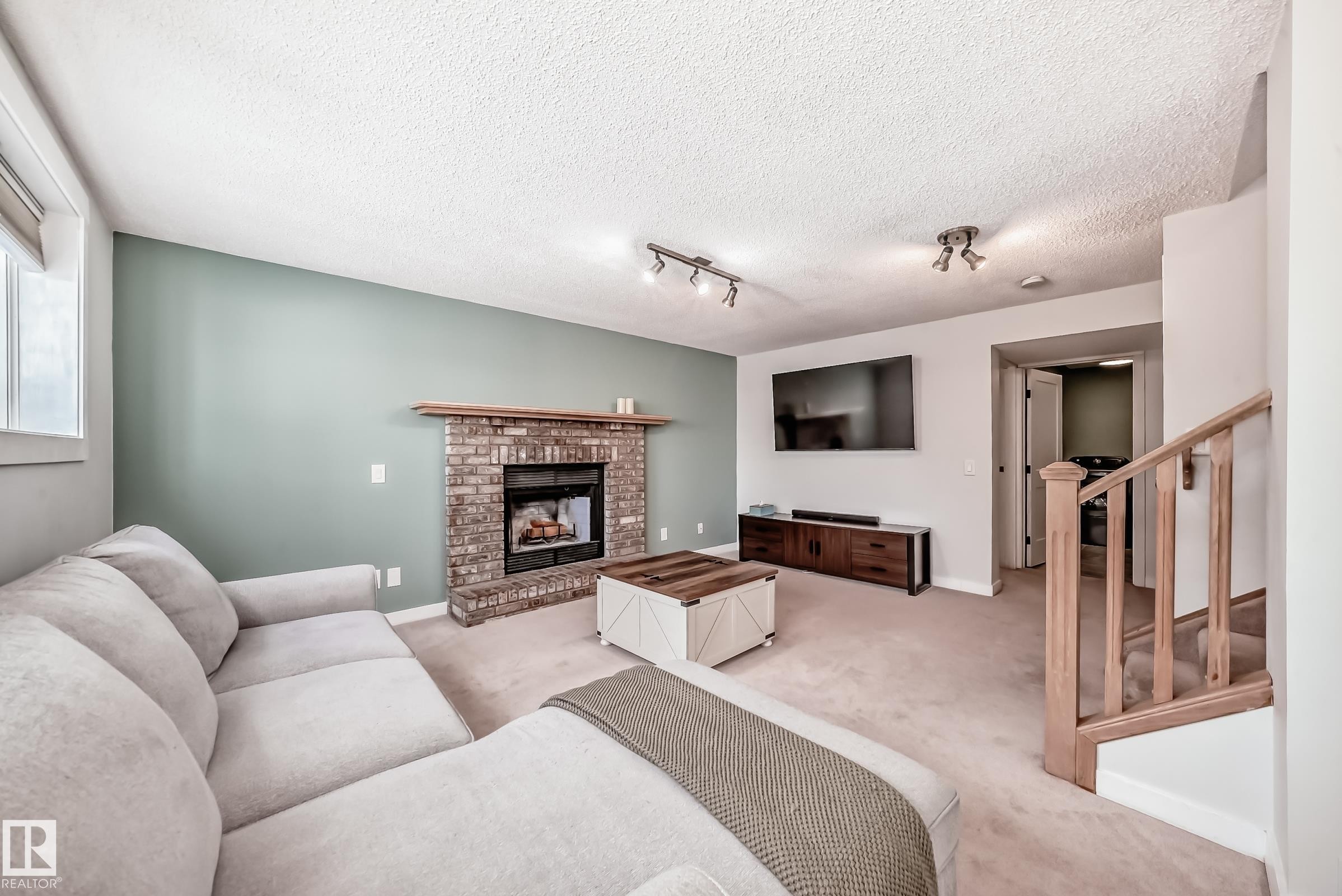 Living area featuring a fireplace, carpet floors, track lighting, and a textured ceiling - 7011 190B Street, Edmonton, AB - Indoor Photo Showing Living Room With Fireplace