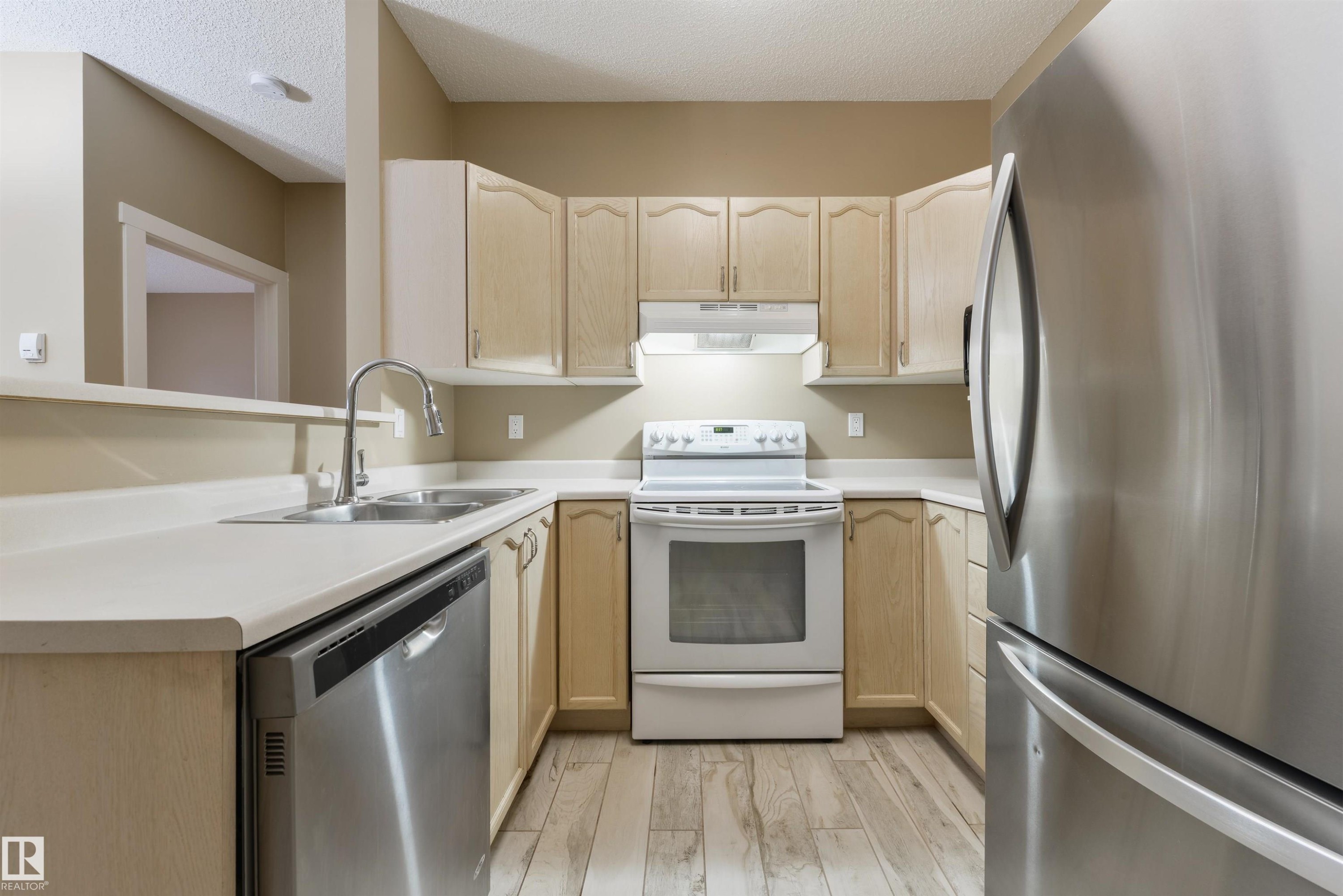 Kitchen with stainless steel appliances, light wood finish cabinets, light countertops, light wood-type flooring, and a textured ceiling - 232 15499 Castle Downs Road, Edmonton, AB - Indoor Photo Showing Kitchen With Double Sink
