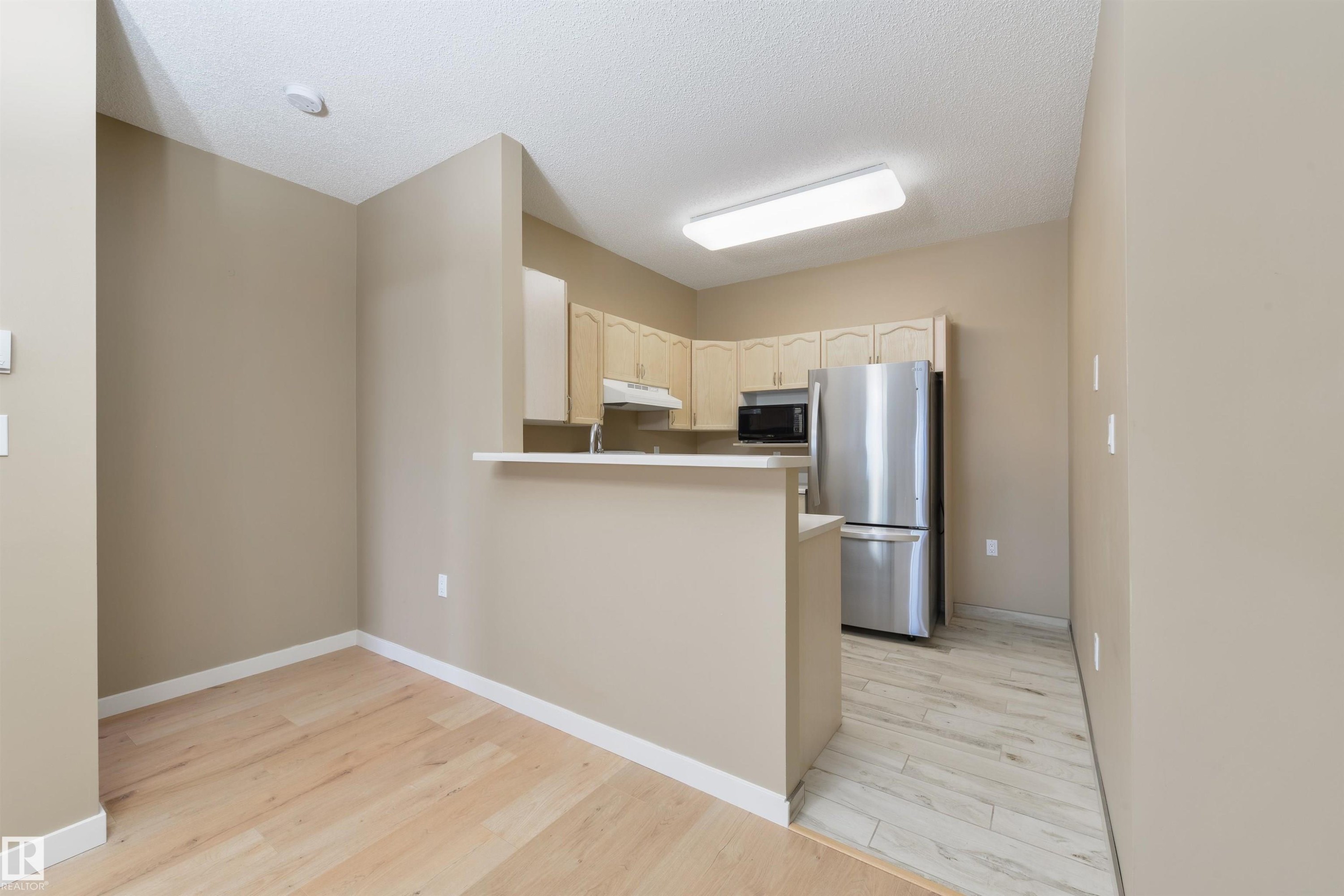 Kitchen with freestanding refrigerator, light wood-type flooring, light countertops, a peninsula, and a textured ceiling - 232 15499 Castle Downs Road, Edmonton, AB - Indoor Photo Showing Other Room