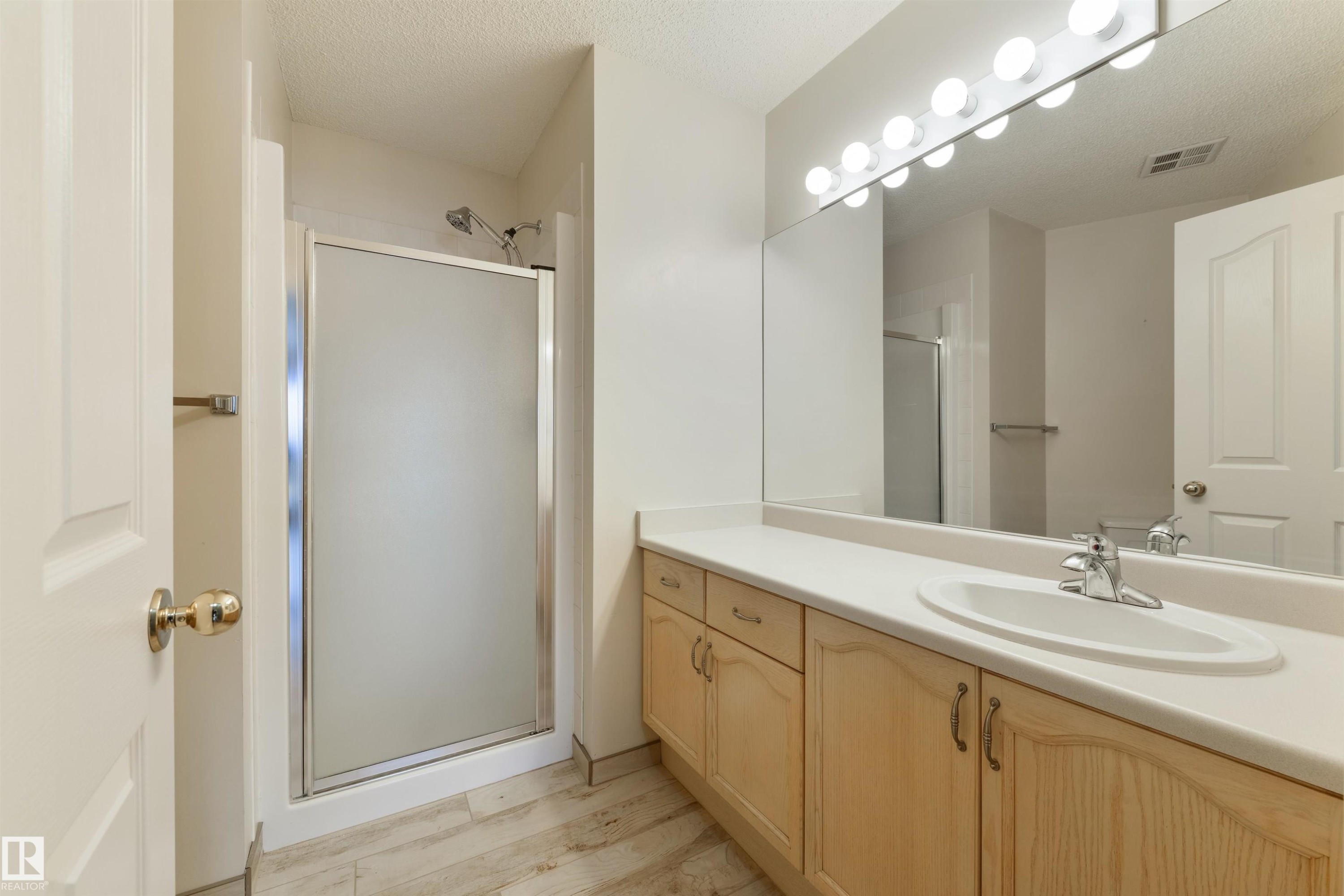 Bathroom with a shower stall, vanity, a textured ceiling, and light wood-style floors - 232 15499 Castle Downs Road, Edmonton, AB - Indoor Photo Showing Bathroom