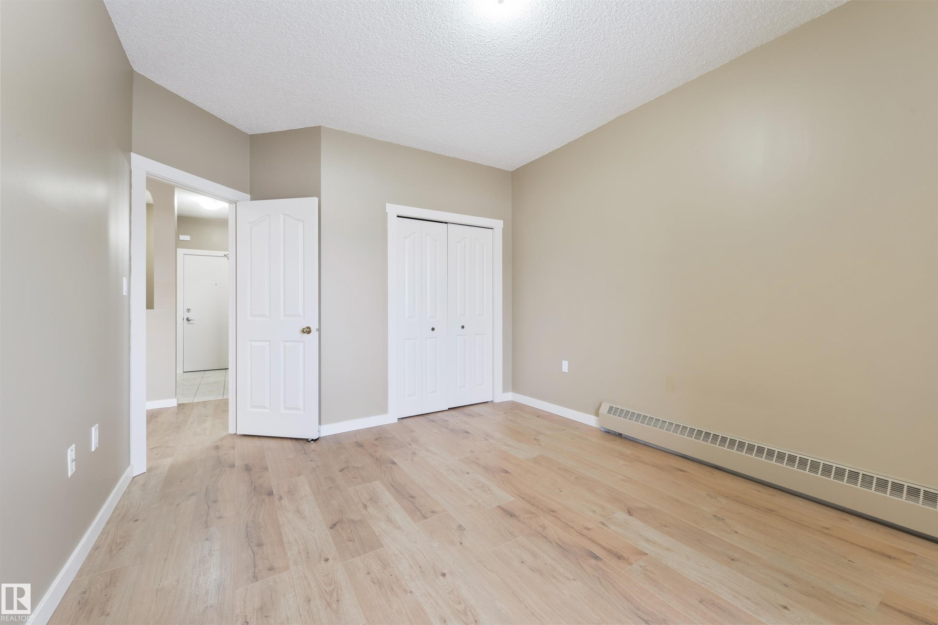 Unfurnished bedroom featuring a baseboard heating unit, light wood-style flooring, a textured ceiling, and a closet - 232 15499 Castle Downs Road, Edmonton, AB - Indoor Photo Showing Other Room