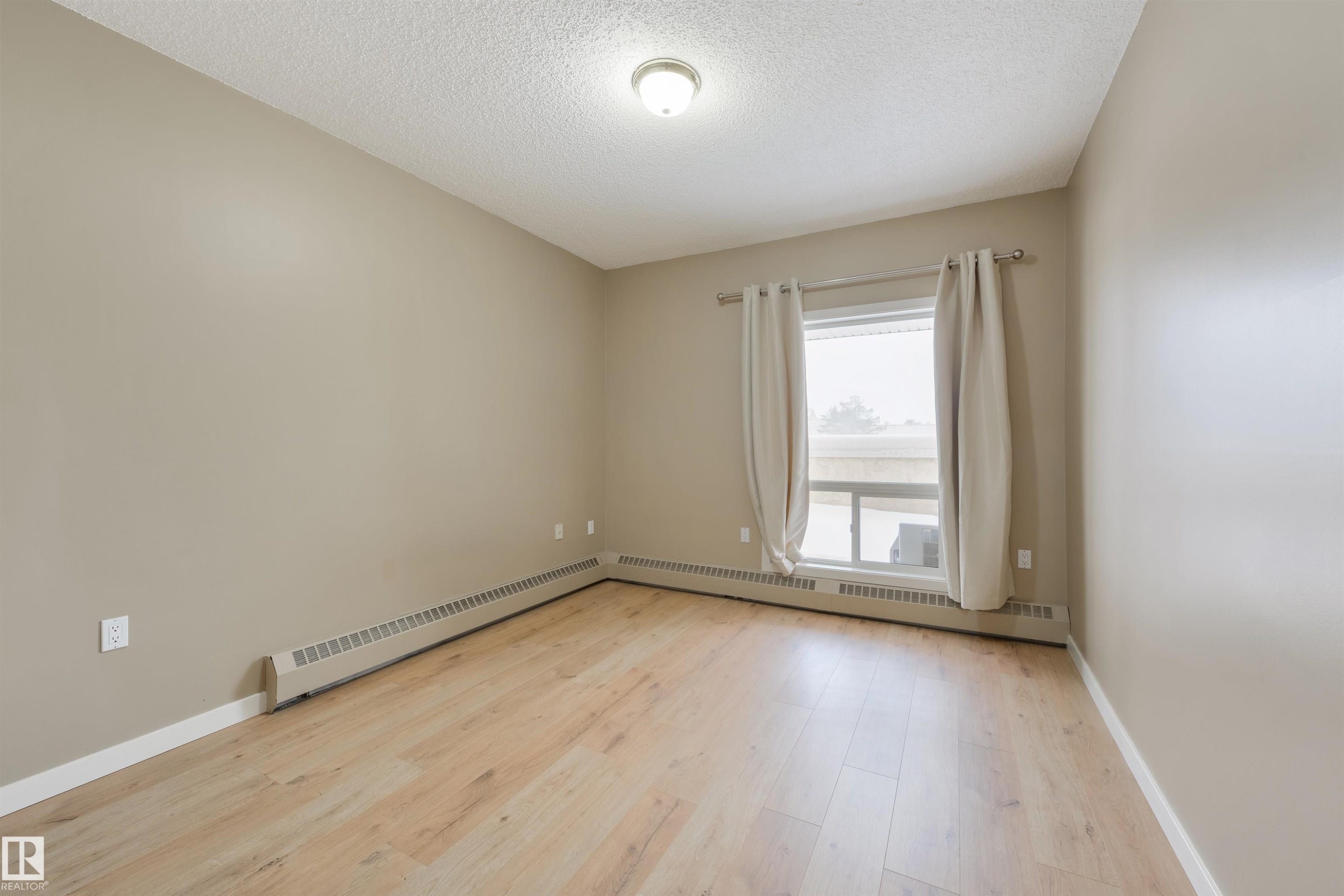 Empty room with light wood-style floors, a baseboard radiator, and a textured ceiling - 232 15499 Castle Downs Road, Edmonton, AB - Indoor Photo Showing Other Room