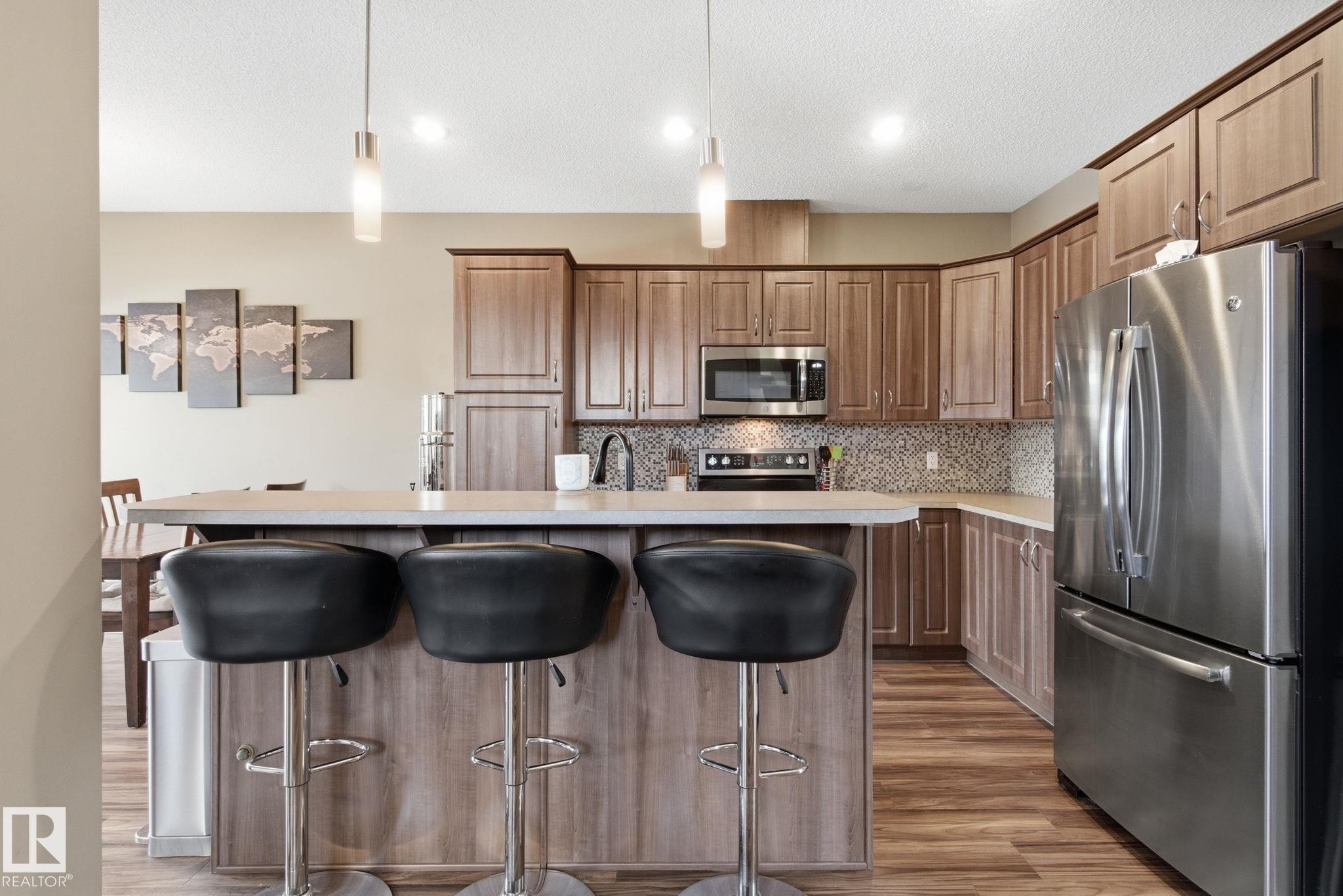 Kitchen with stainless steel appliances, pendant lighting, a breakfast bar area, light countertops, and a textured ceiling - 3087 Arthurs Crescent, Edmonton, AB - Indoor Photo Showing Kitchen With Stainless Steel Kitchen With Upgraded Kitchen
