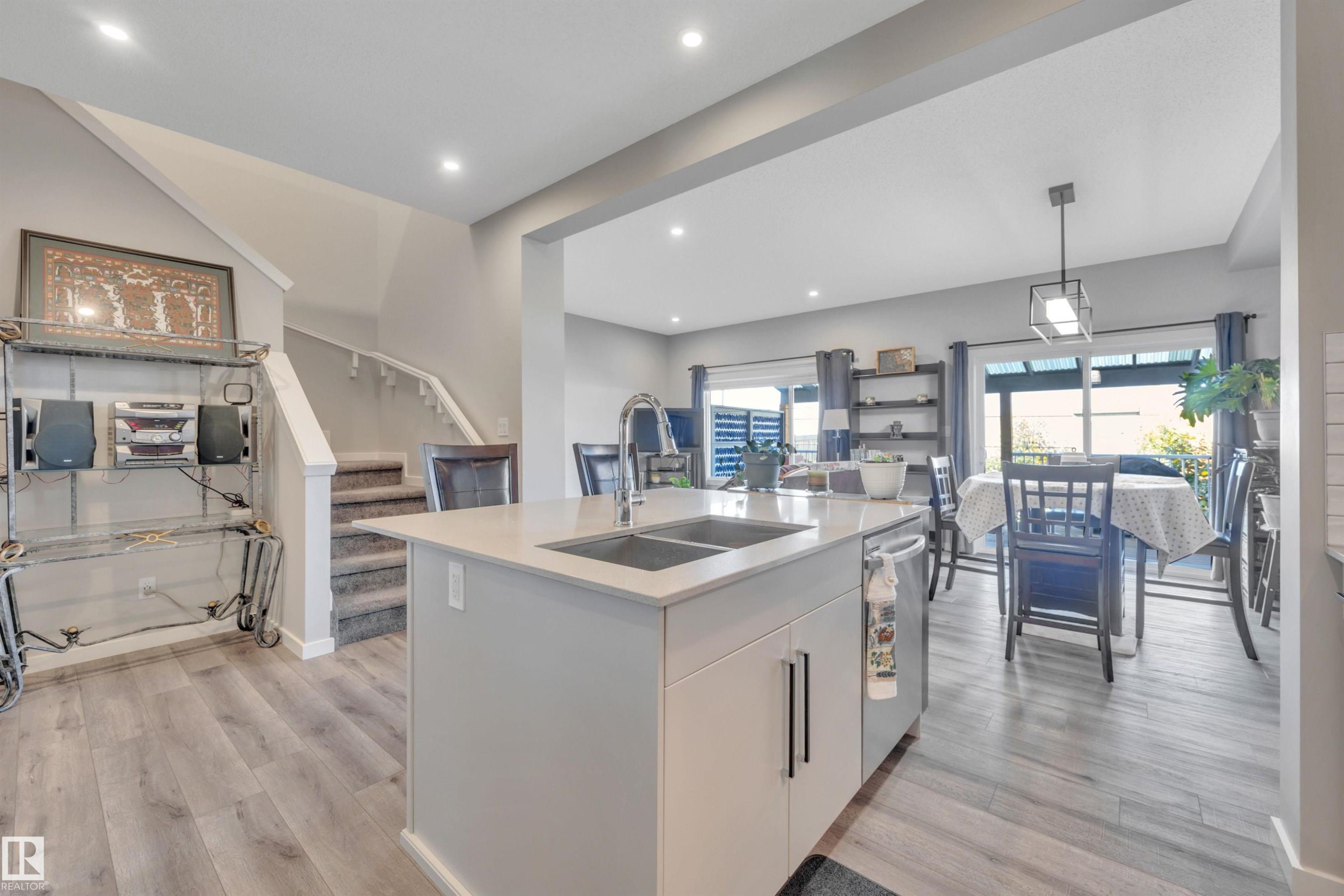 Kitchen with white cabinets, a kitchen island with sink, hanging light fixtures, light wood-type flooring, and stainless steel dishwasher - 157 Larch Crescent, Leduc, AB - Indoor Photo Showing Kitchen With Double Sink