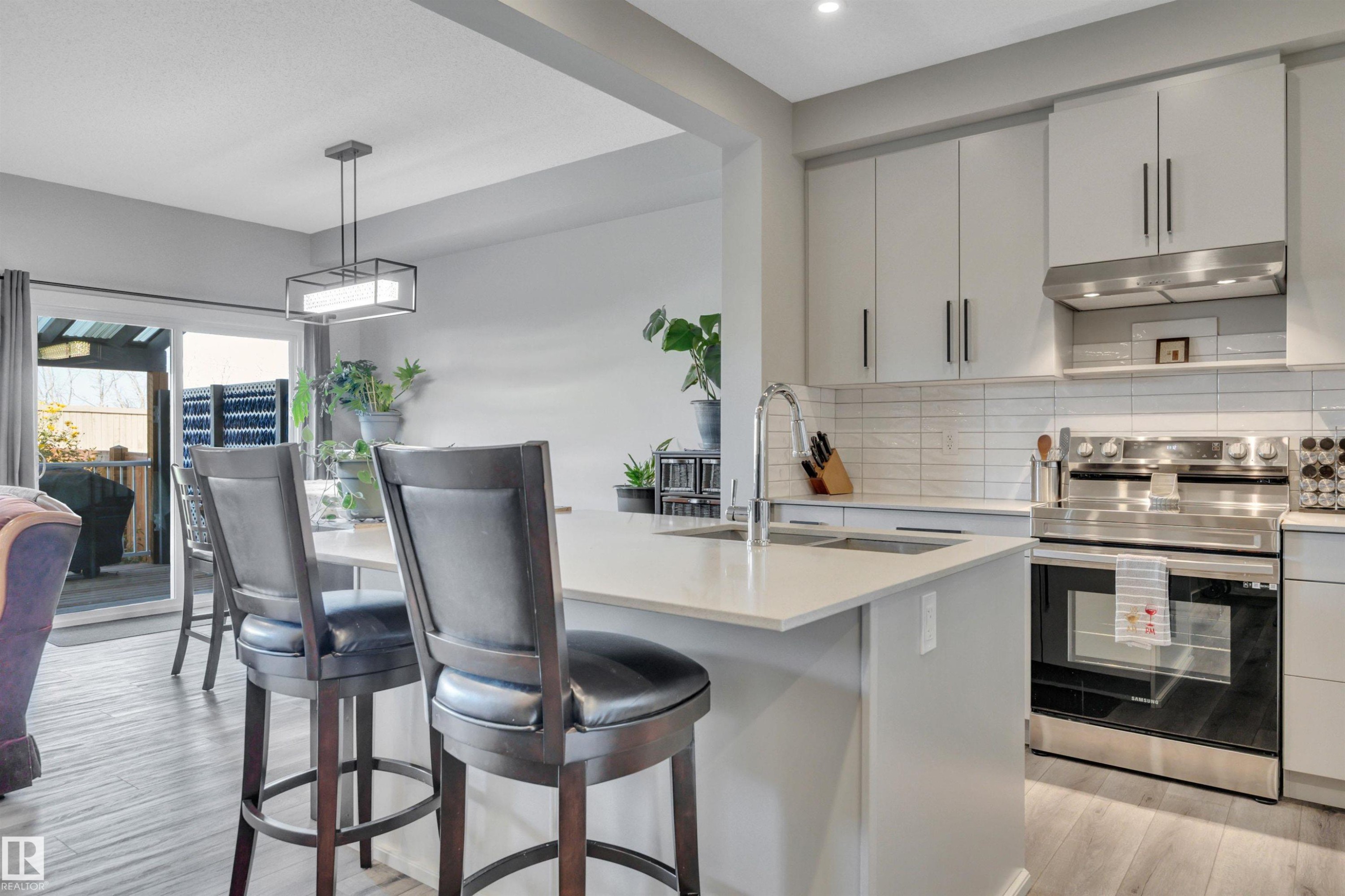Kitchen featuring electric range, light wood-style flooring, tasteful backsplash, pendant lighting, and a breakfast bar - 157 Larch Crescent, Leduc, AB - Indoor Photo Showing Kitchen With Upgraded Kitchen