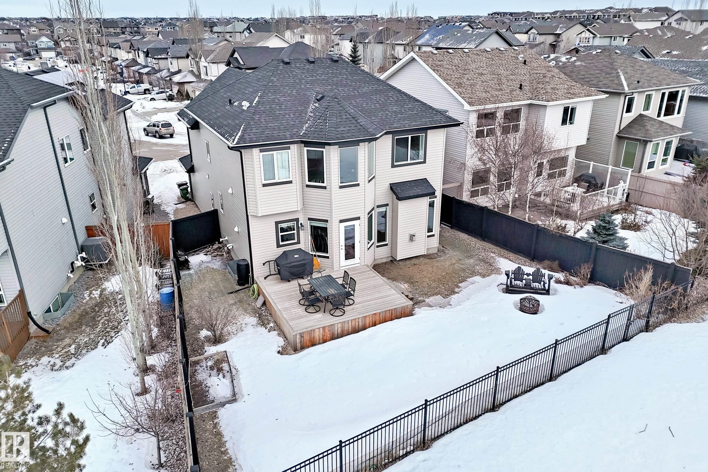 Snow covered rear of property featuring a fire pit, a wooden deck, a fenced backyard, and a residential view - 1908 69 Street, Edmonton, AB - Outdoor