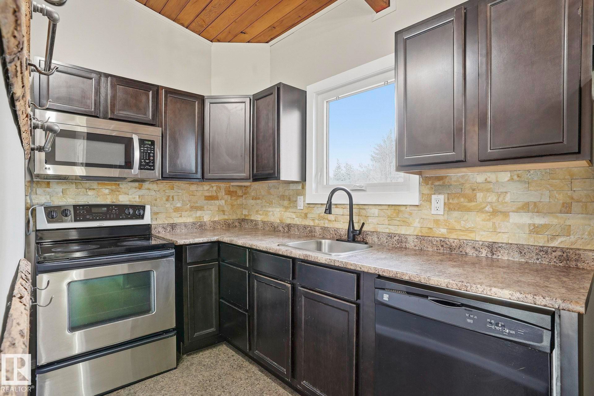 Kitchen featuring stainless steel appliances, wooden ceiling, decorative backsplash, dark aggregate flooring, and light countertops - Edmonton, AB - Indoor Photo Showing Kitchen
