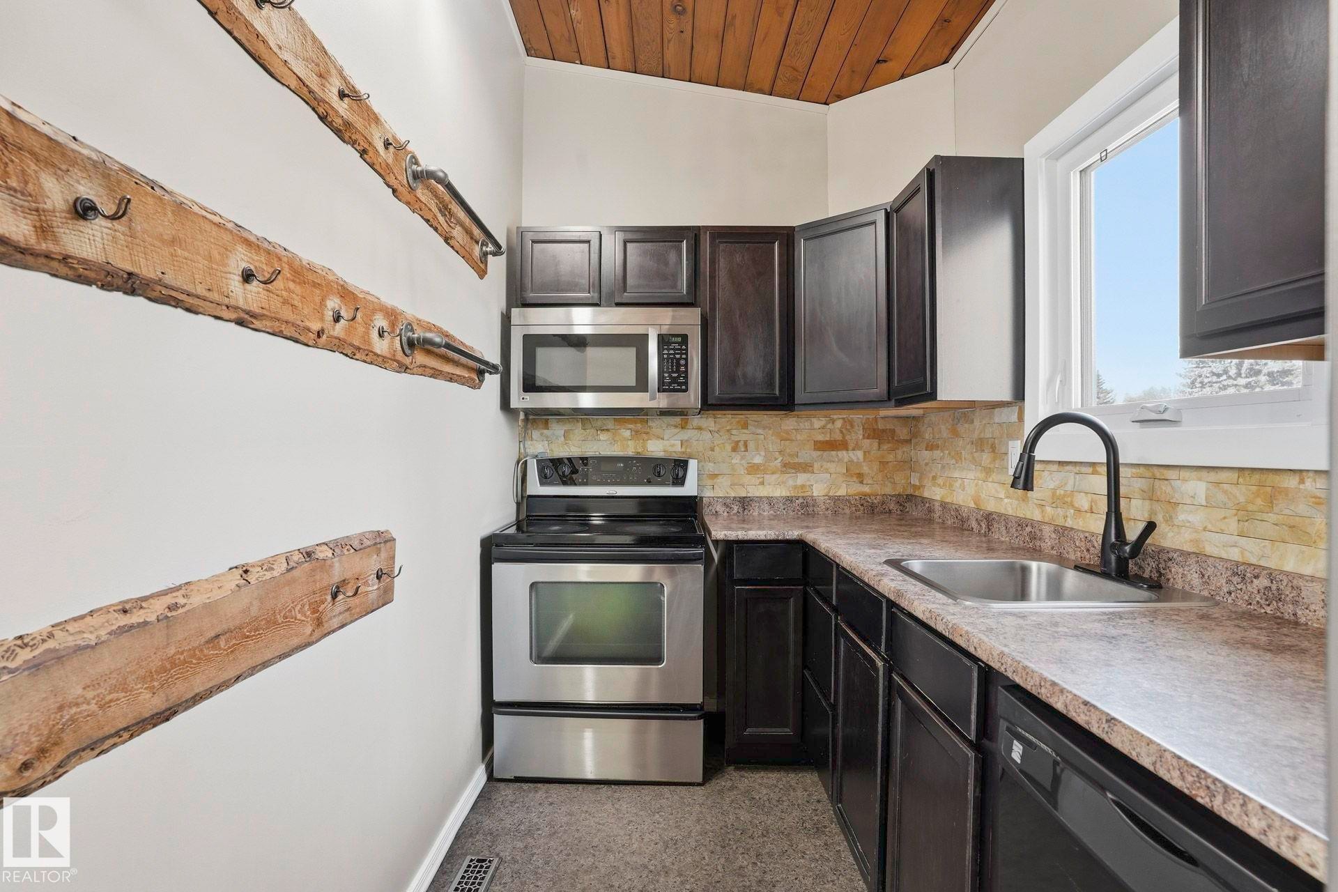 Kitchen with stainless steel appliances, wood ceiling, backsplash, and dark wood finish cabinets - Edmonton, AB - Indoor Photo Showing Kitchen